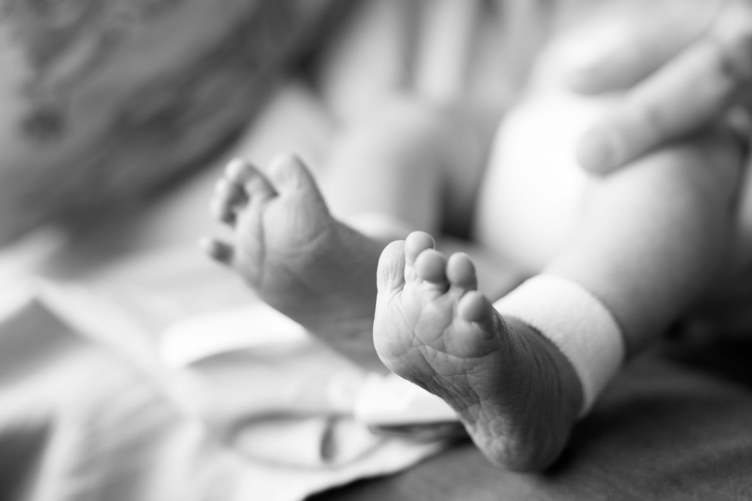 Black and white close-up photo of newborn baby feet with hospital ID bracelet.