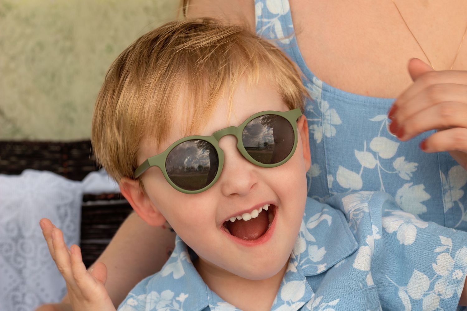 Happy boy in green sunglasses and floral shirt smiling outdoors, perfect kids sunglasses style.
