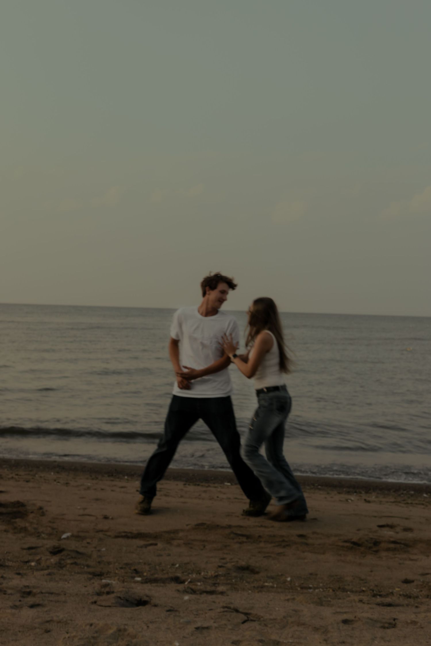 A couple dancing together on a sandy beach at dusk, with calm ocean waves in the background.