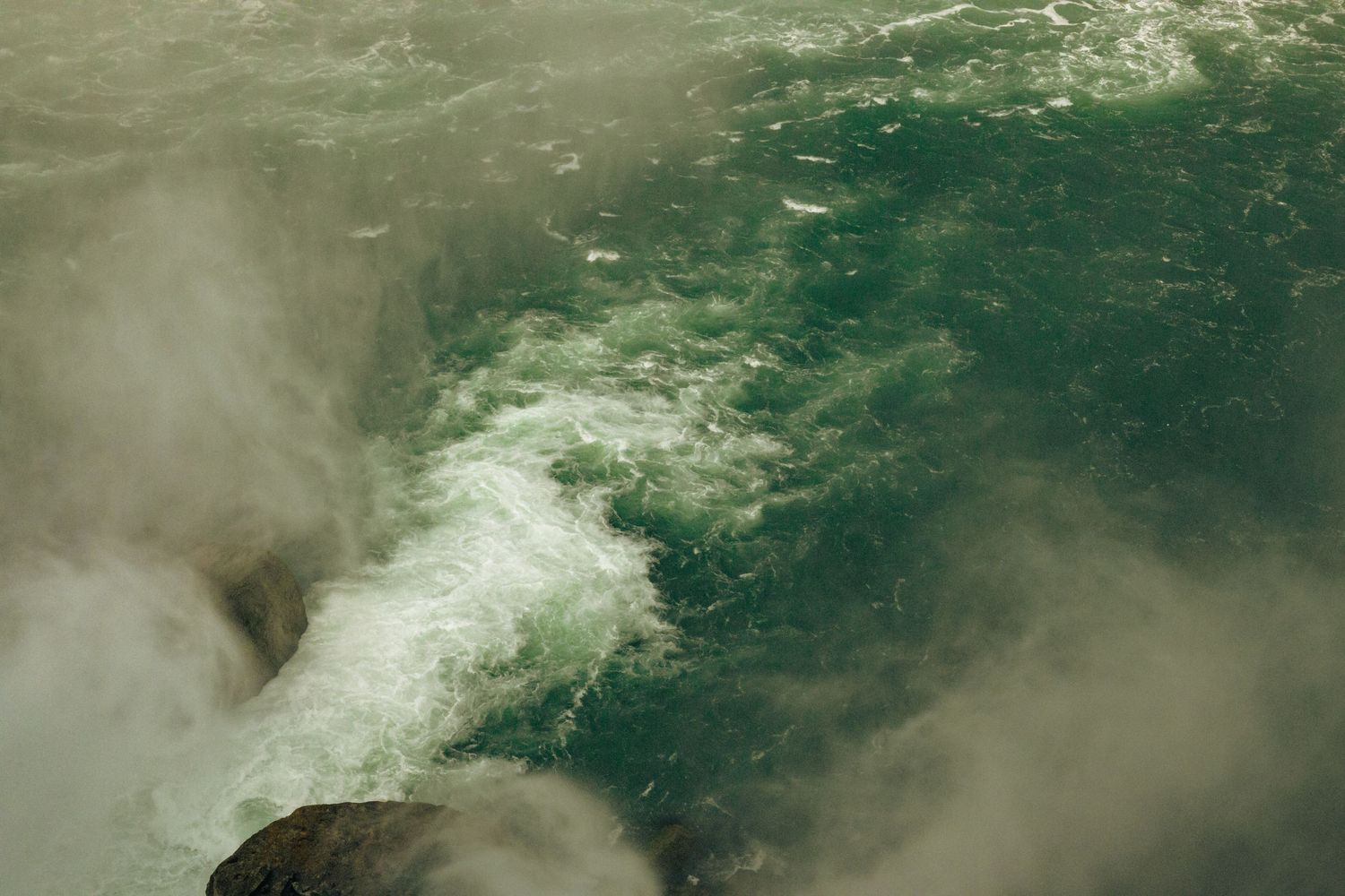 Aerial view of powerful rushing waterfall with misty white foam and turbulent green water below.