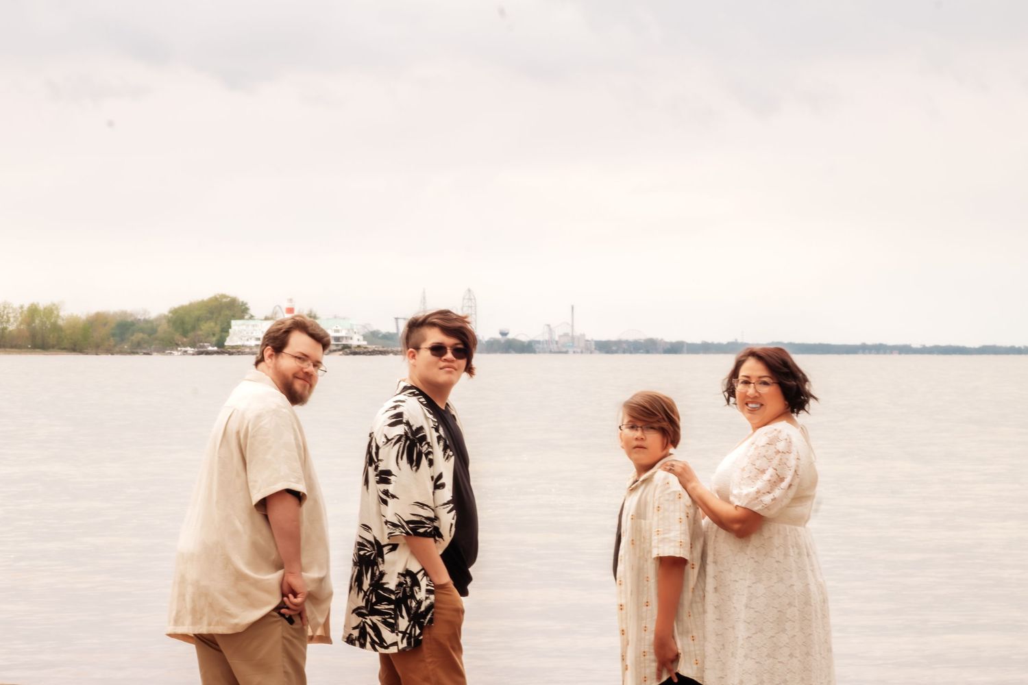 Family of four posing together on a waterfront shore with calm water and distant ships in the background.