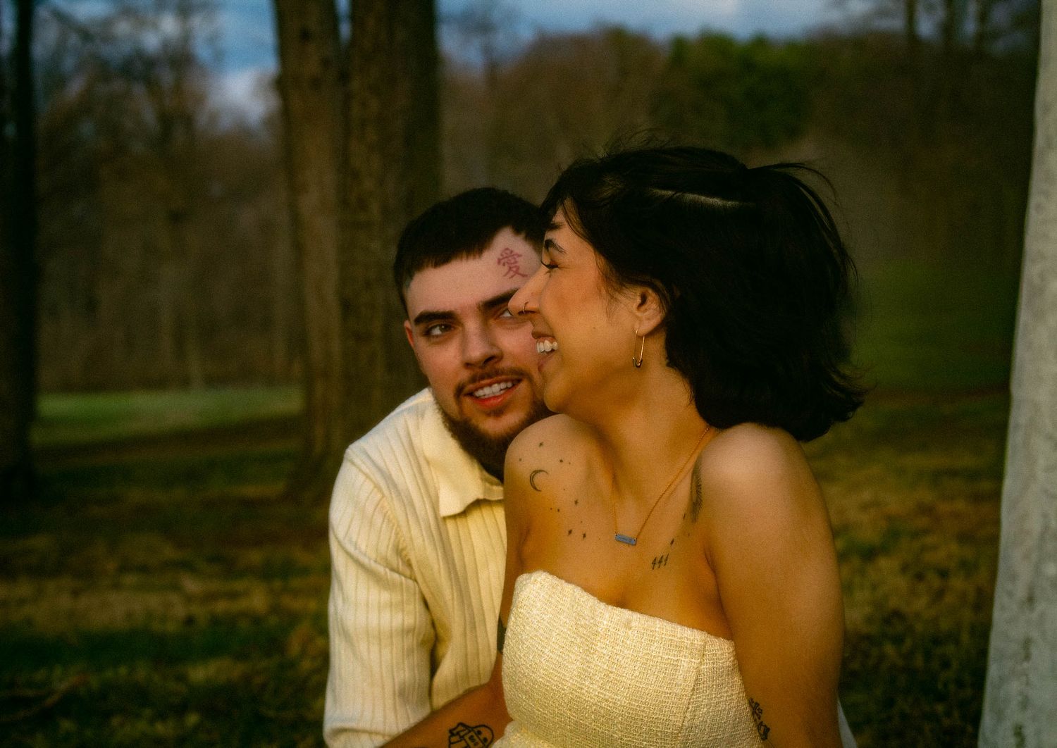 A romantic wedding couple embraces outdoors in a natural setting during golden hour lighting.