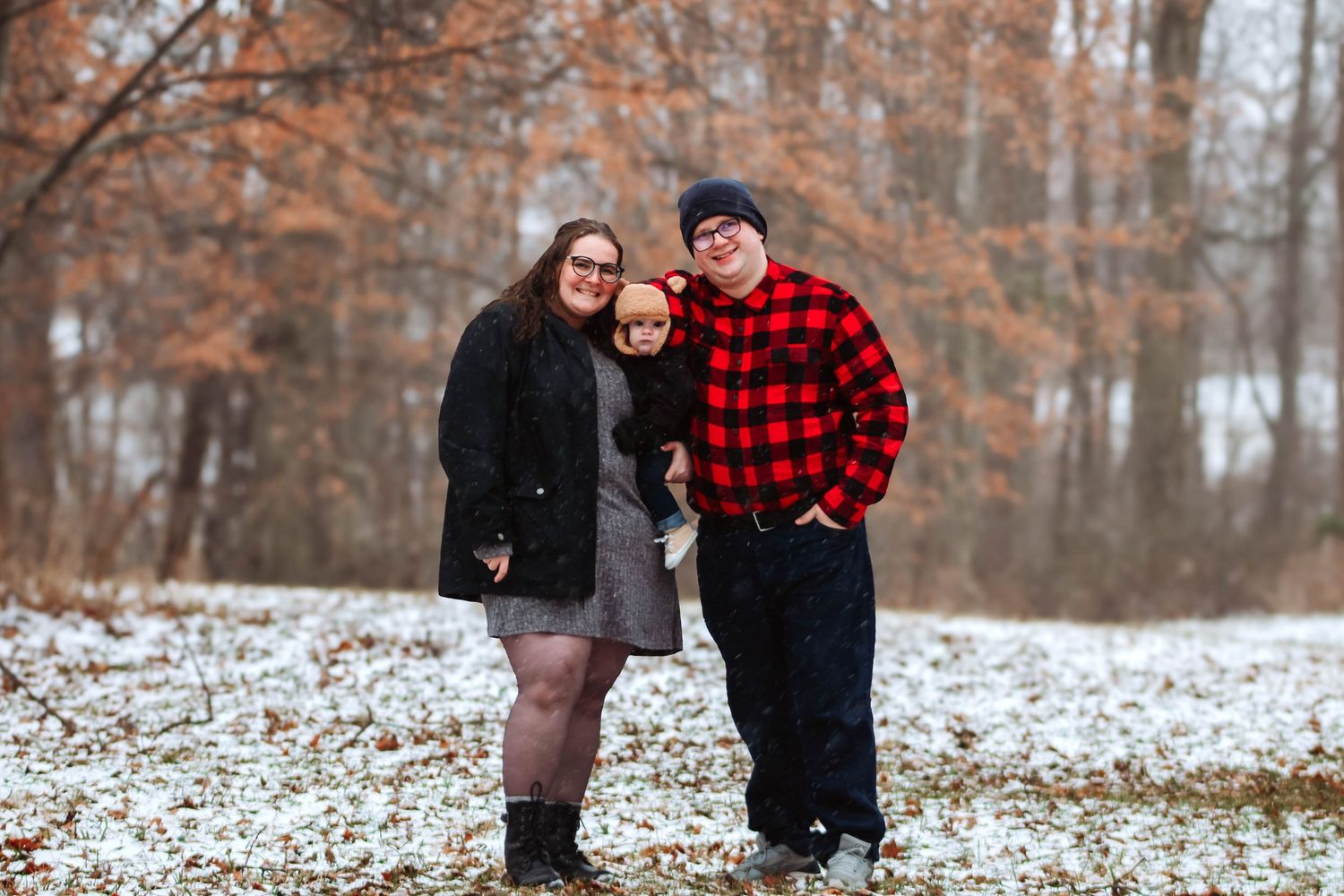 Winter engagement photos with couple in buffalo plaid and black coats on snowy ground.