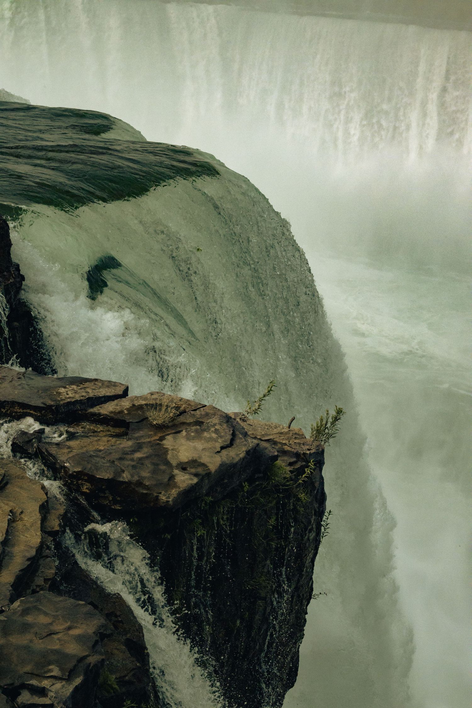 Aerial view of massive waterfall cascading over rocky cliff edge with misty green water below.
