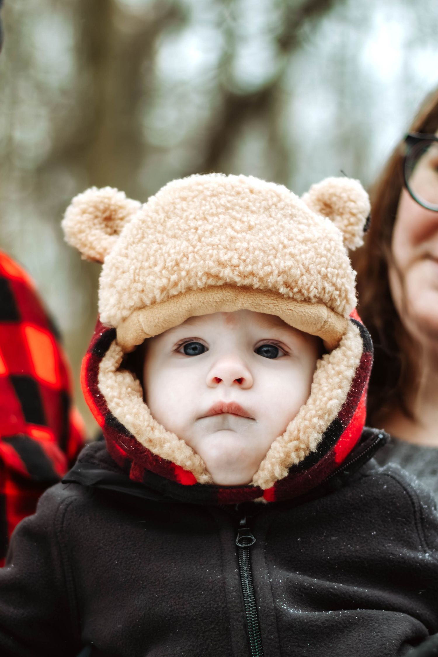 Baby wearing cozy brown winter hat and black jacket in snowy weather.