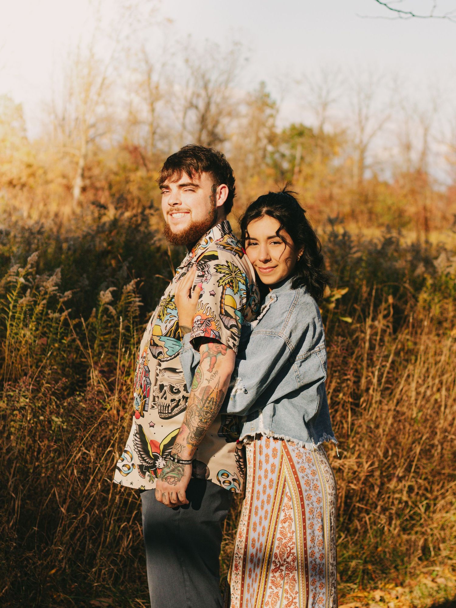 A couple embraces in a field of tall grass during golden hour.
