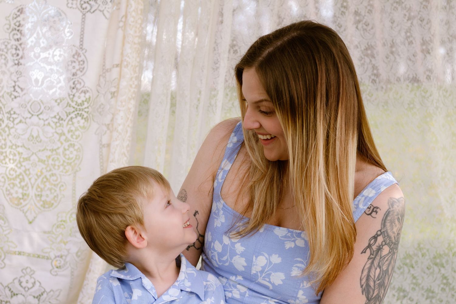 A smiling mother and young son in matching blue outfits share a tender moment together indoors.