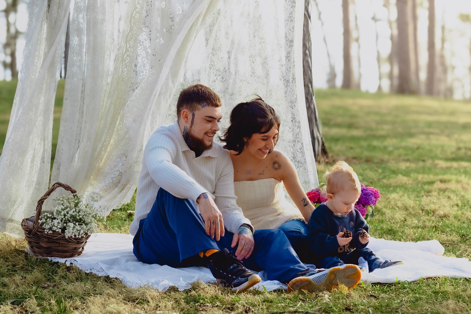 A family enjoys quality time together on a white blanket in a grassy outdoor setting during a sunny day.