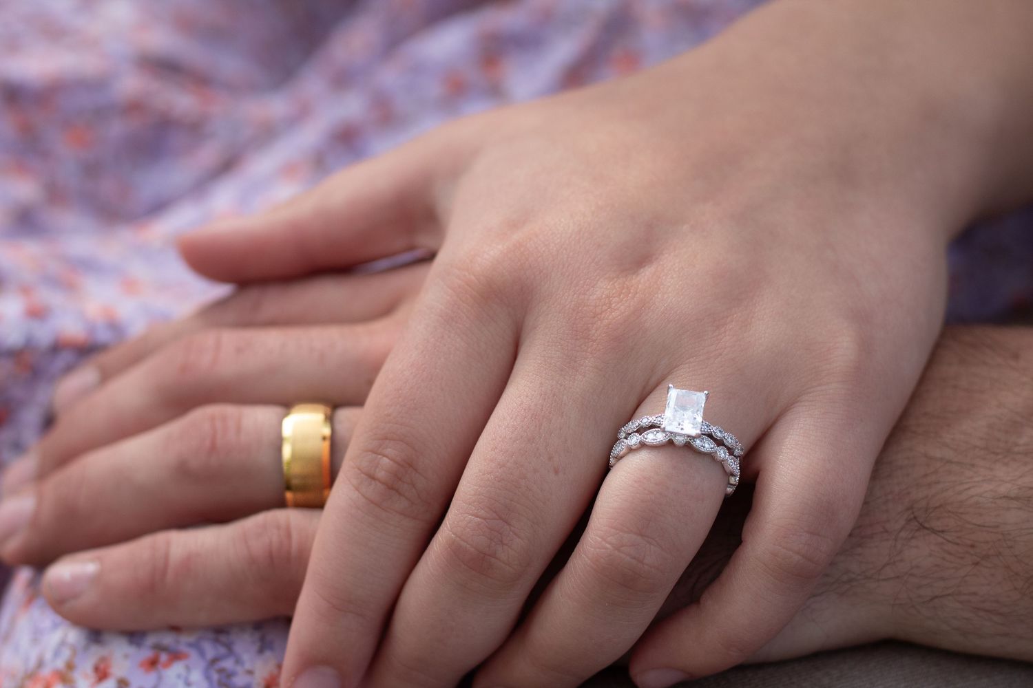 Close up of hands with wedding rings against floral fabric.