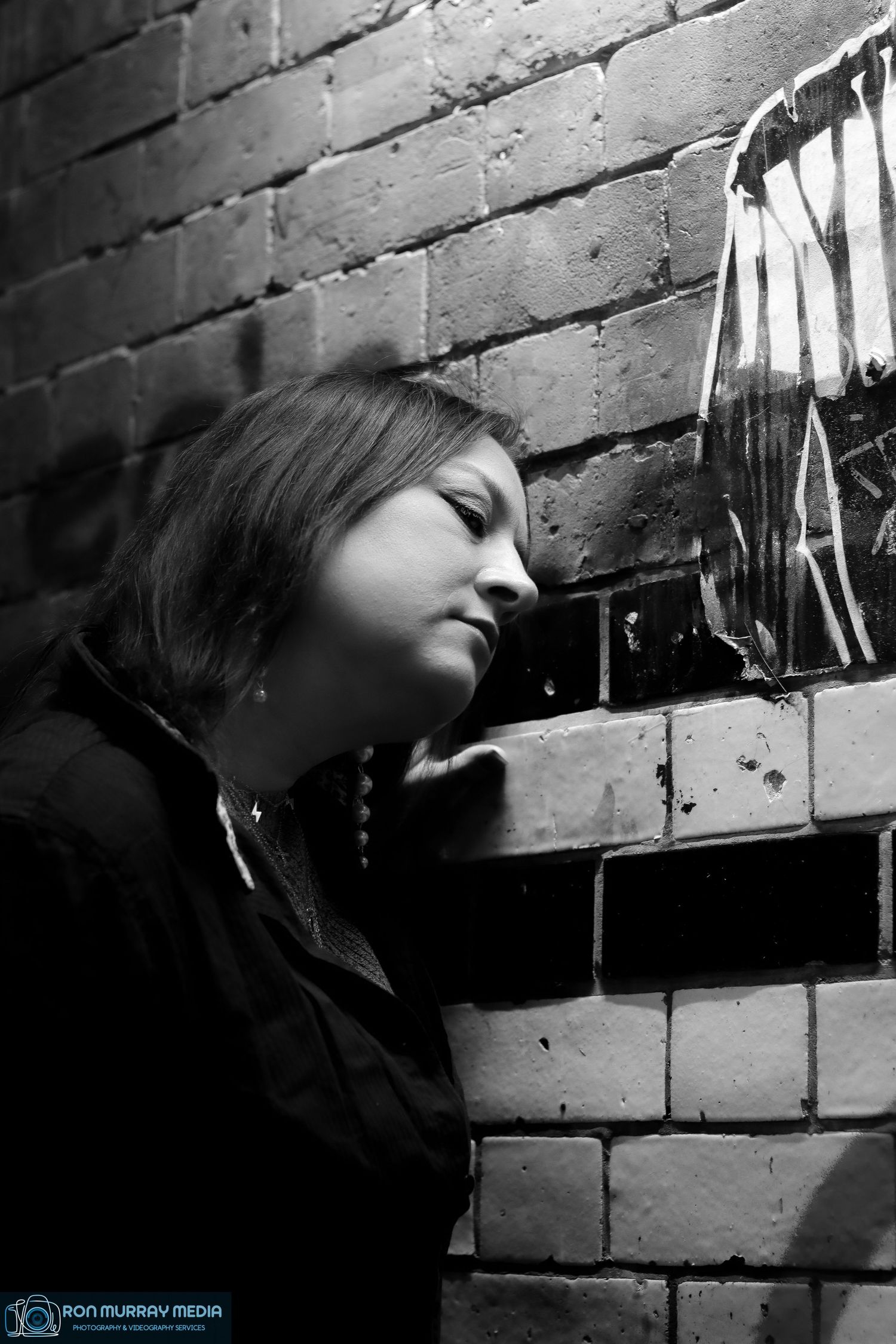 Dramatic black and white portrait against textured brick wall.