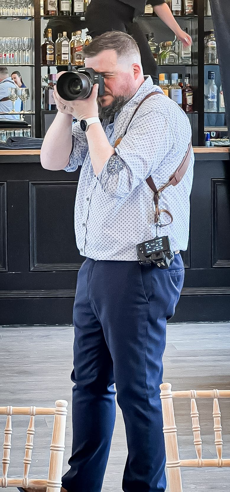Professional photographer in suspenders taking pictures at a bar venue.
