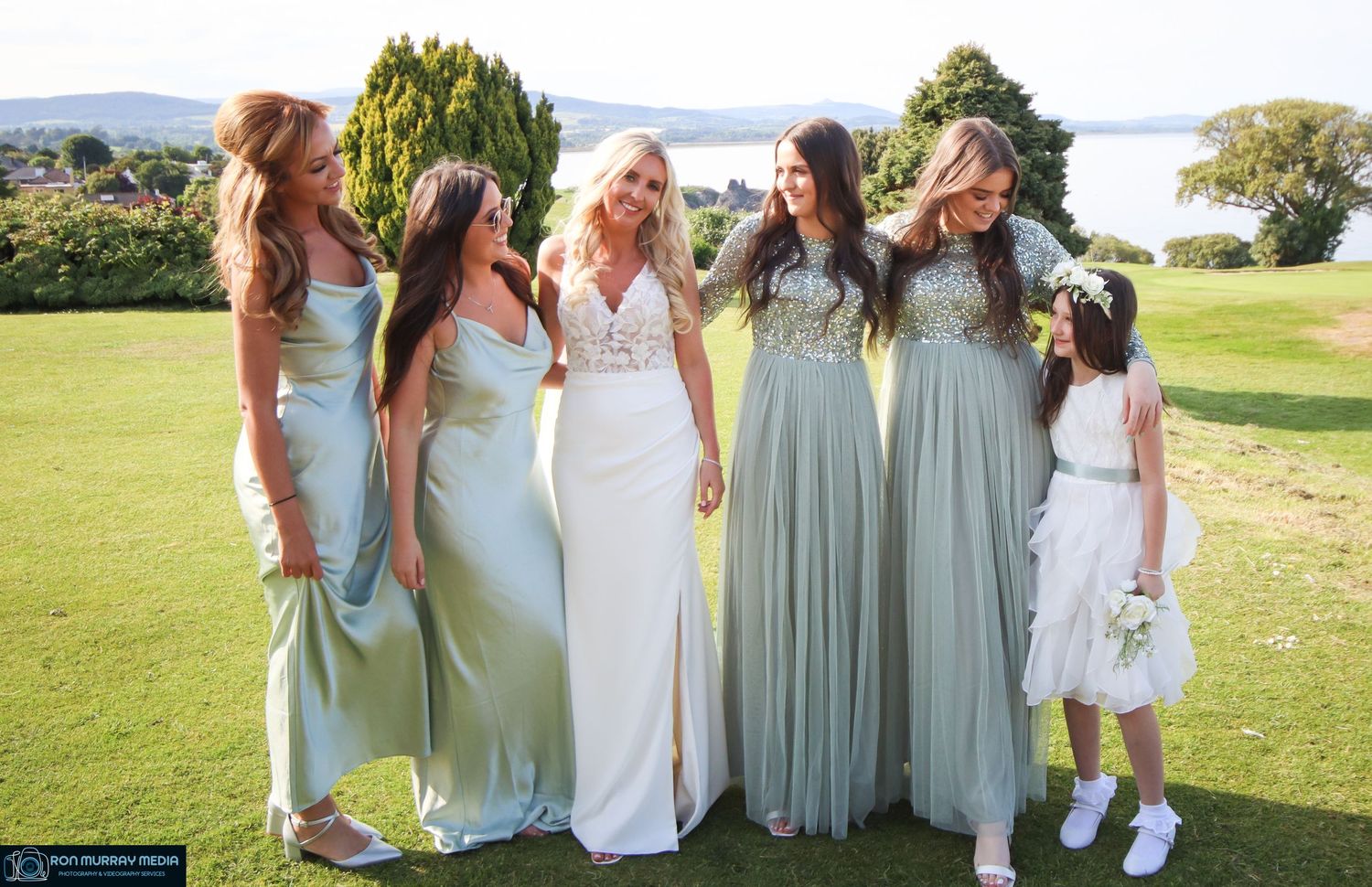 Wedding party in coordinated white and mint green dresses posing on grass.