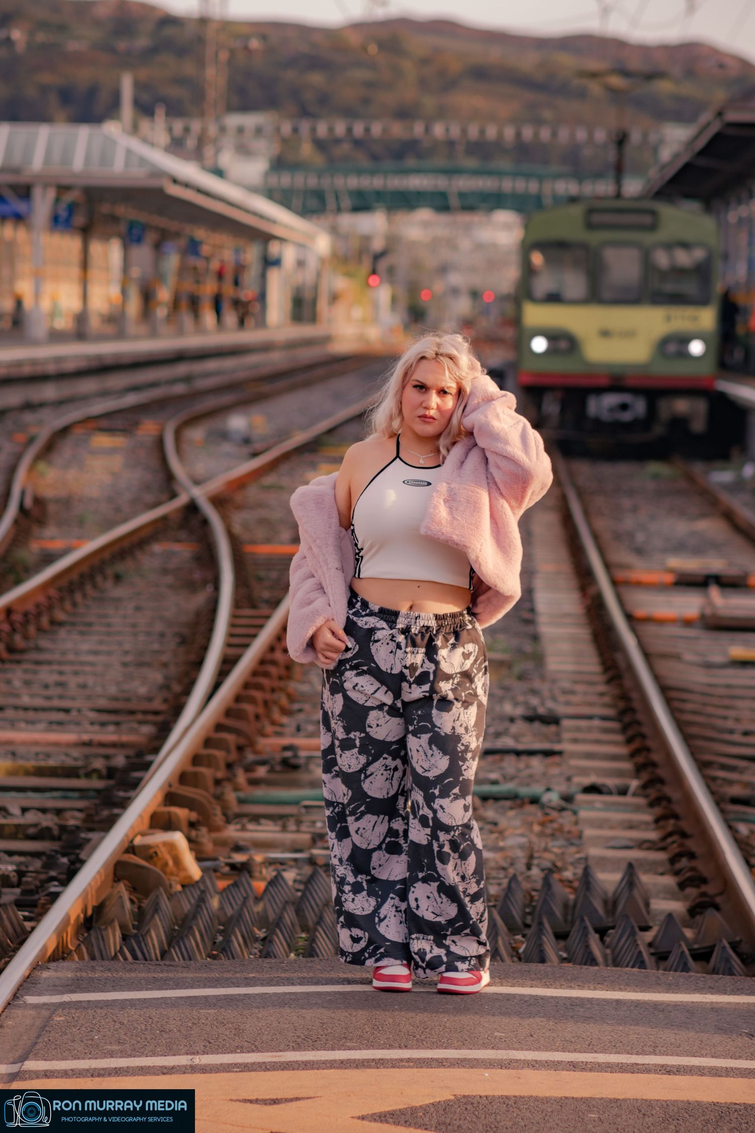 Person in athletic wear posing on railroad tracks at sunset.