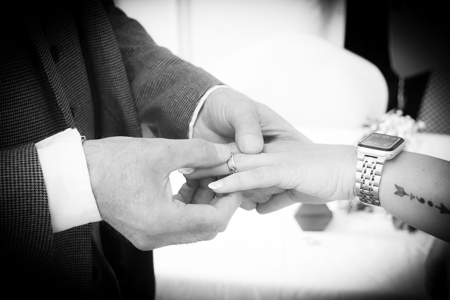 Black and white image showing hands exchanging rings in an intimate wedding moment.