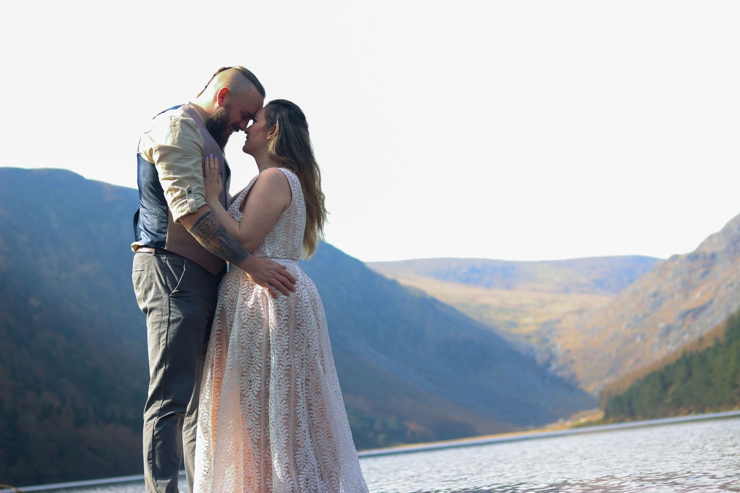 Romantic couple embracing by a scenic mountain lake at sunset.