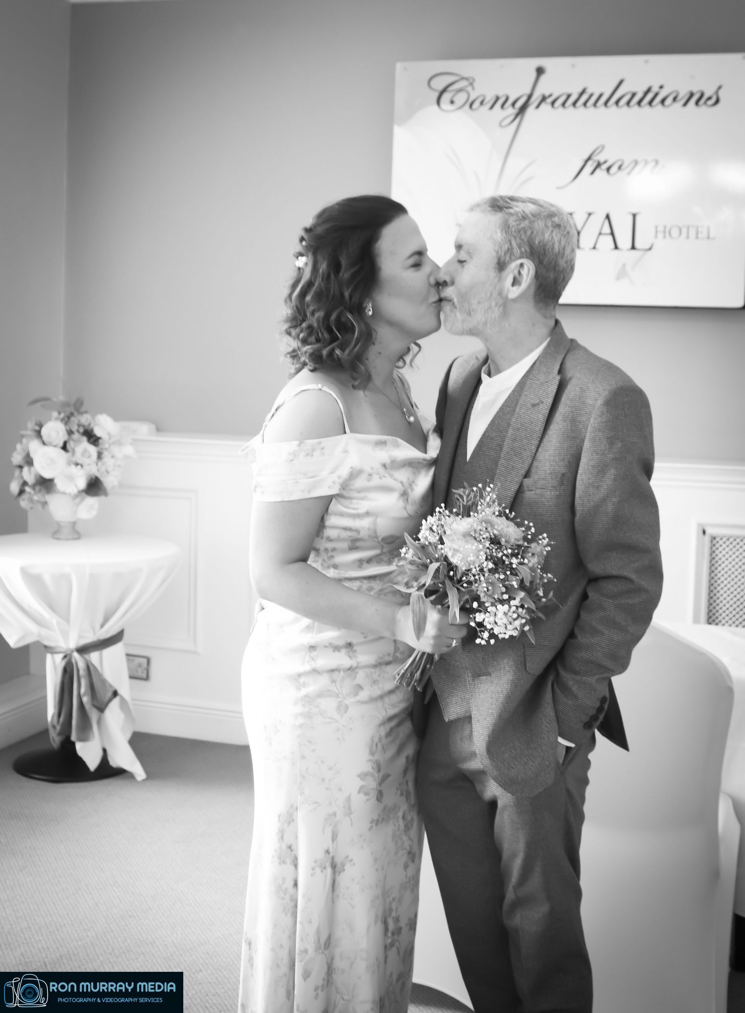 A couple shares an intimate moment in front of a congratulations sign at their wedding celebration.