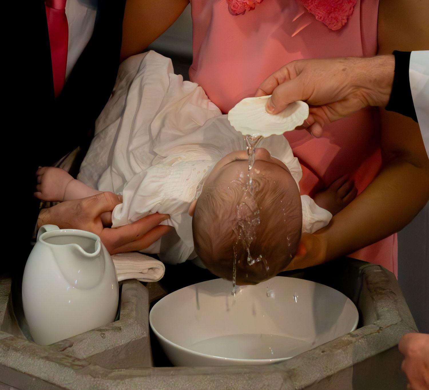 Baby being baptized with water poured from a white vessel during christening ceremony.