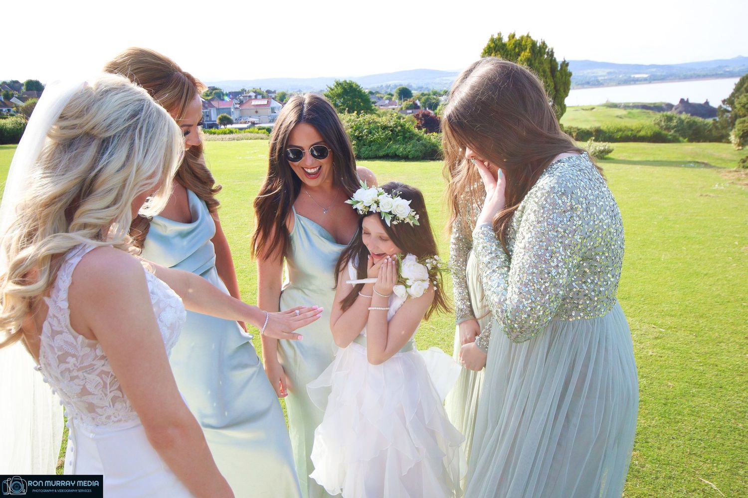 Bridal party wearing pastel dresses celebrating outdoors on a sunny day.