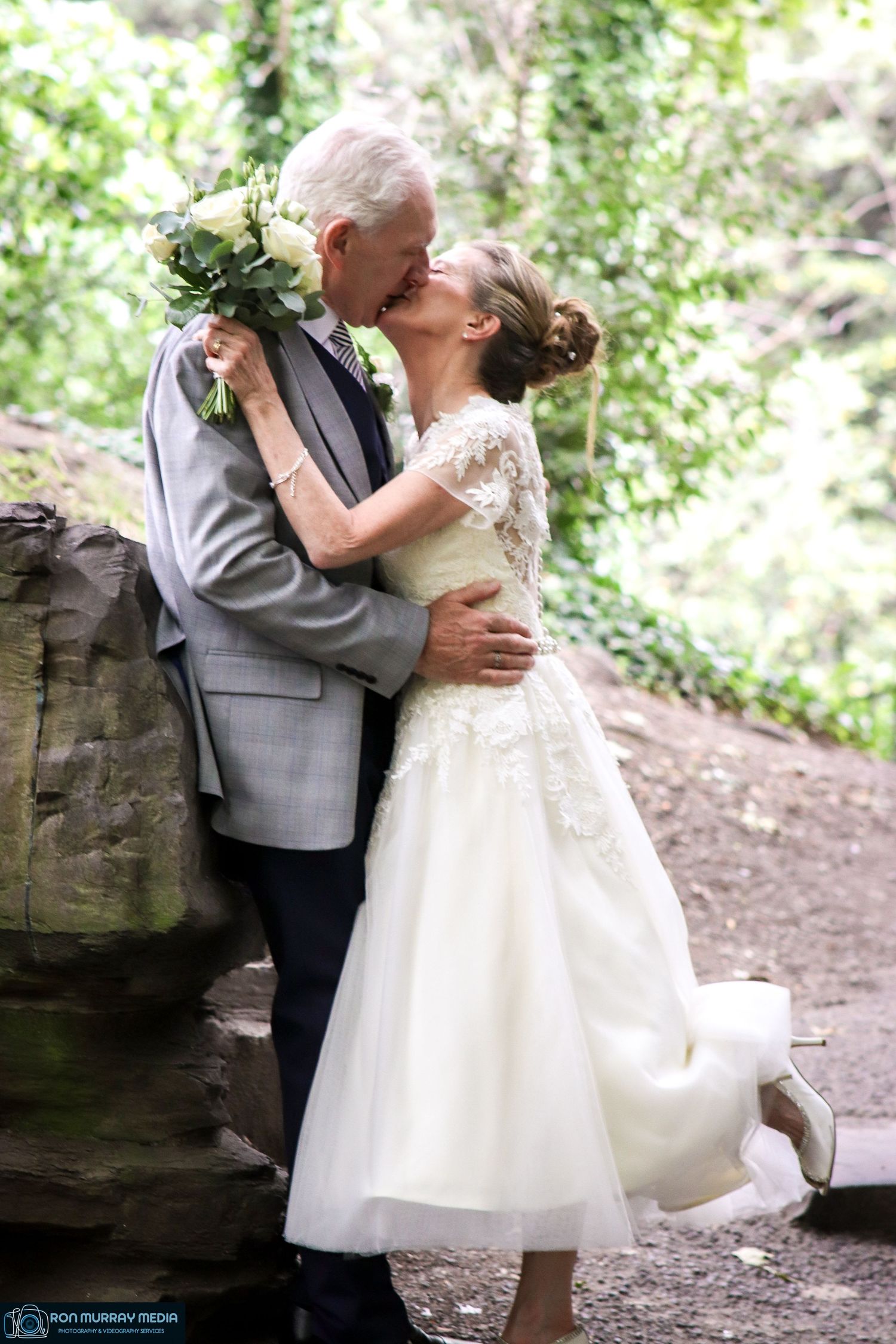 Romantic wedding couple embracing on woodland path in elegant attire.