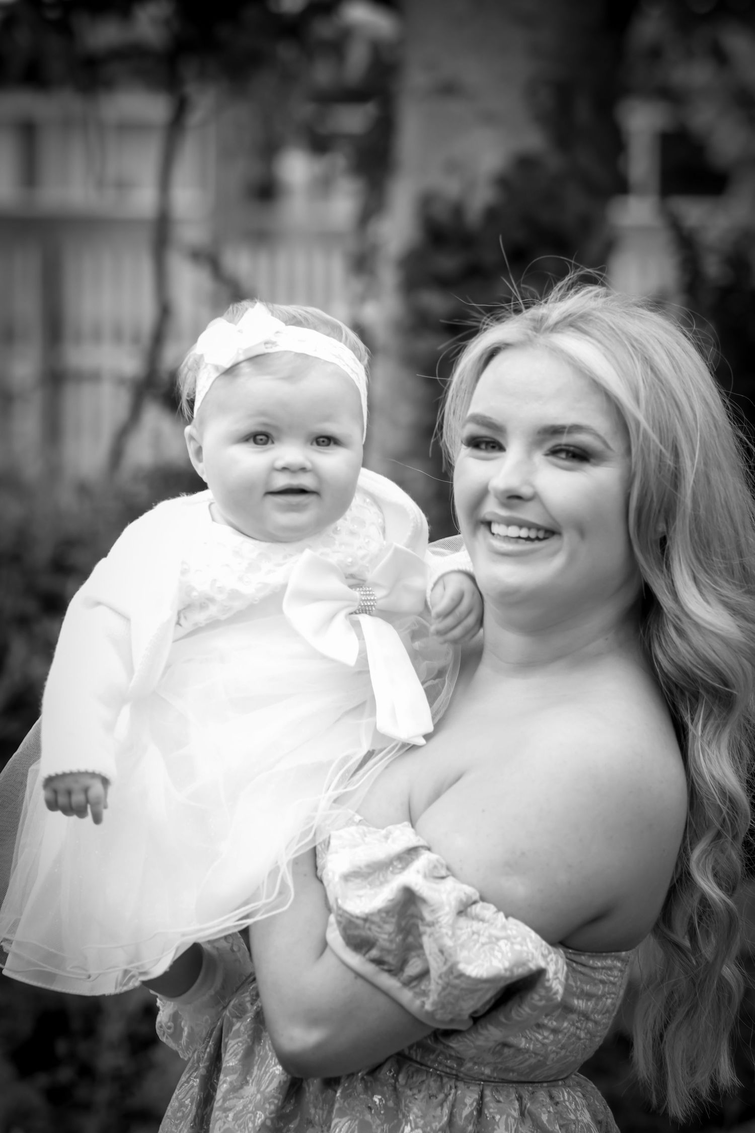 Black and white portrait of a baby with her mother in white christening robes.
