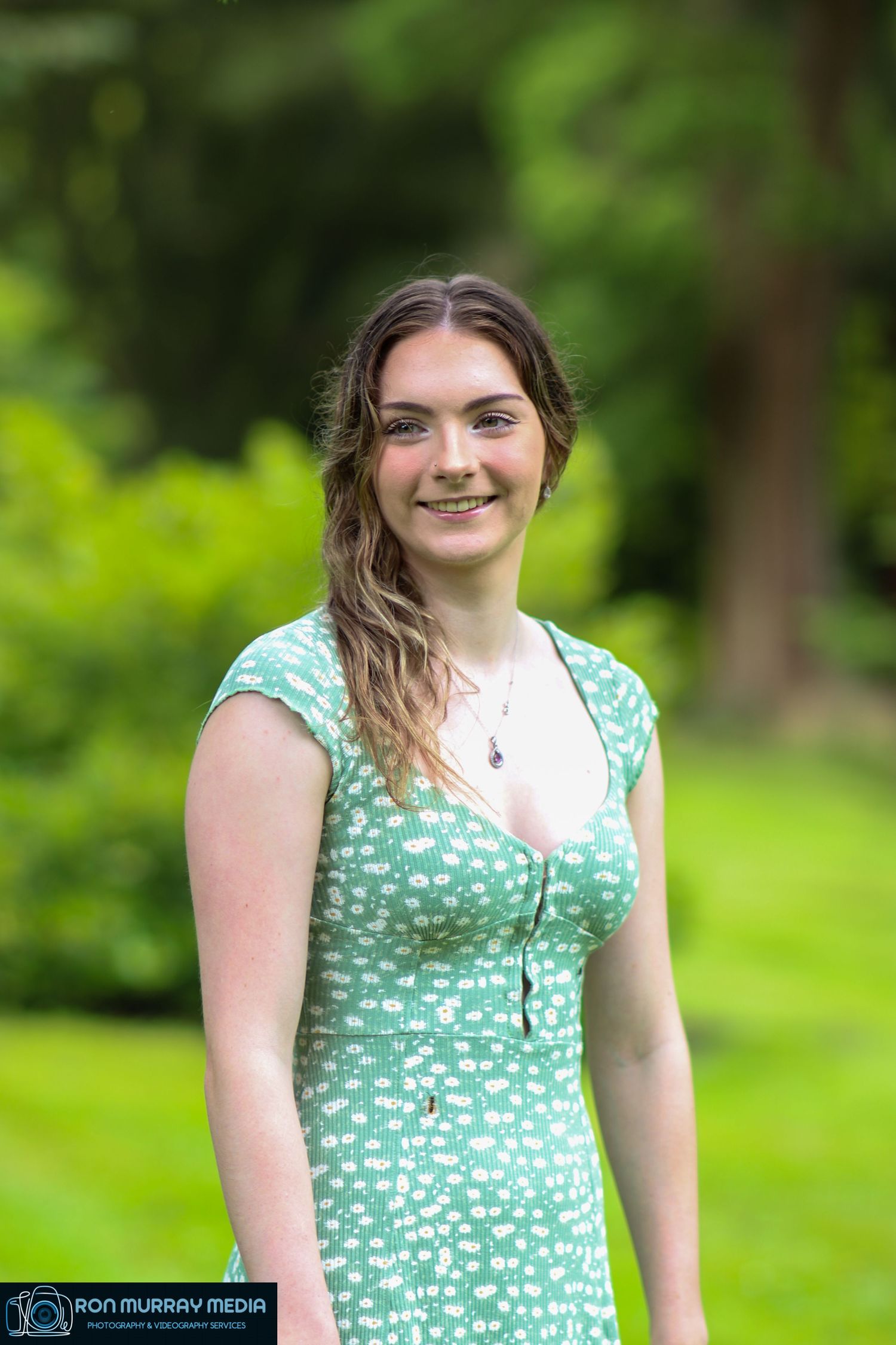A person in a mint green floral dress poses outdoors in a lush green park setting.