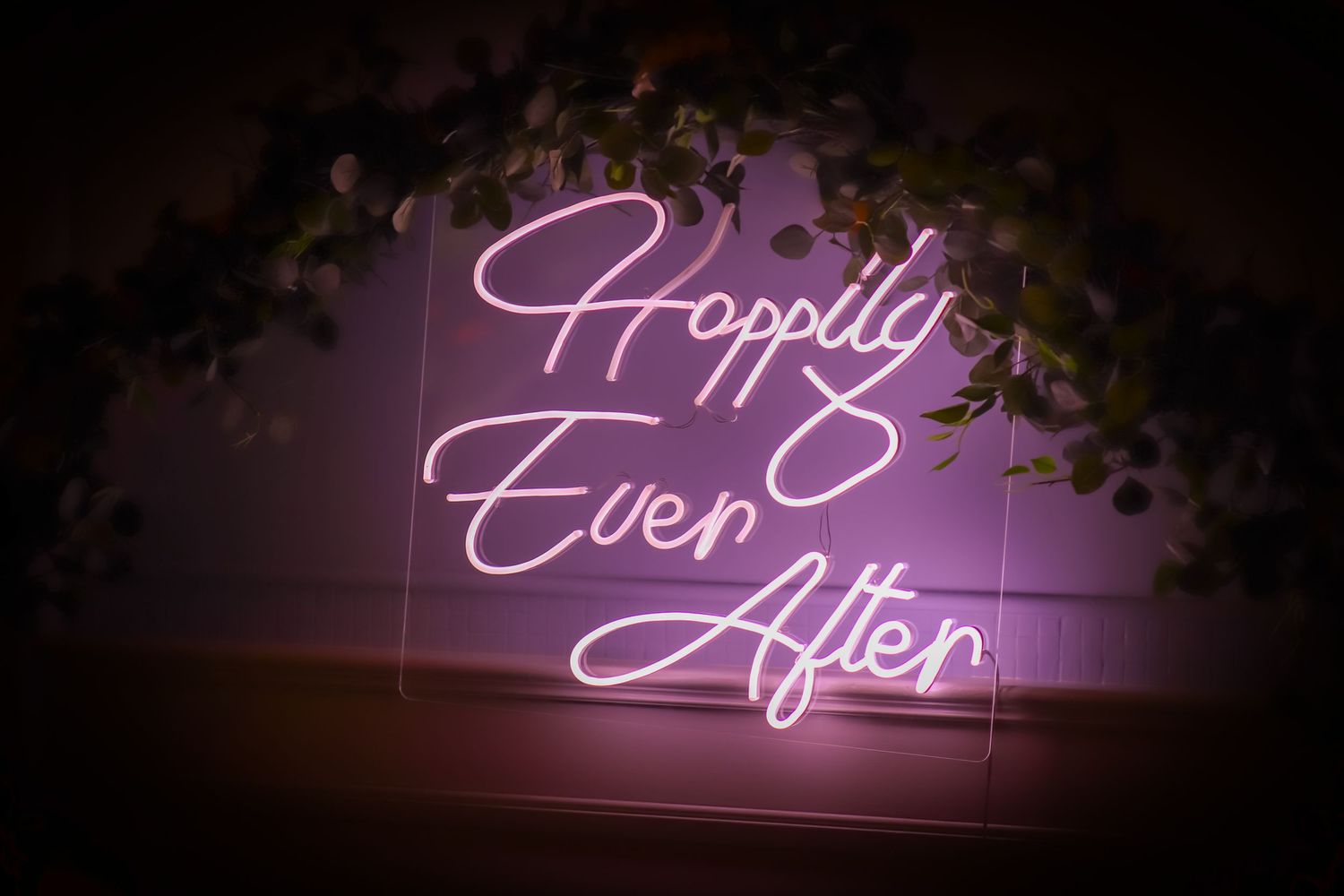 Purple neon sign reading 'Happily Ever After' with decorative greenery.