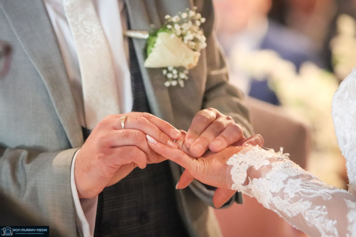 Close-up of hands exchanging wedding rings during ceremony with delicate lace details.