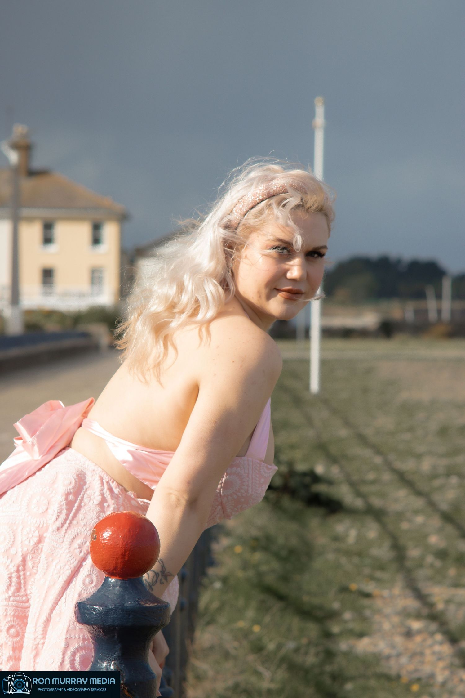 Person in pink dress lying in grassy field with houses in background.