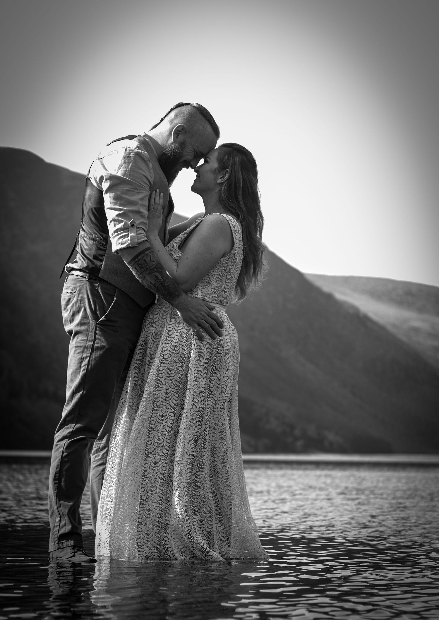 Dramatic black and white photos of a couple embracing in mountain lake waters.