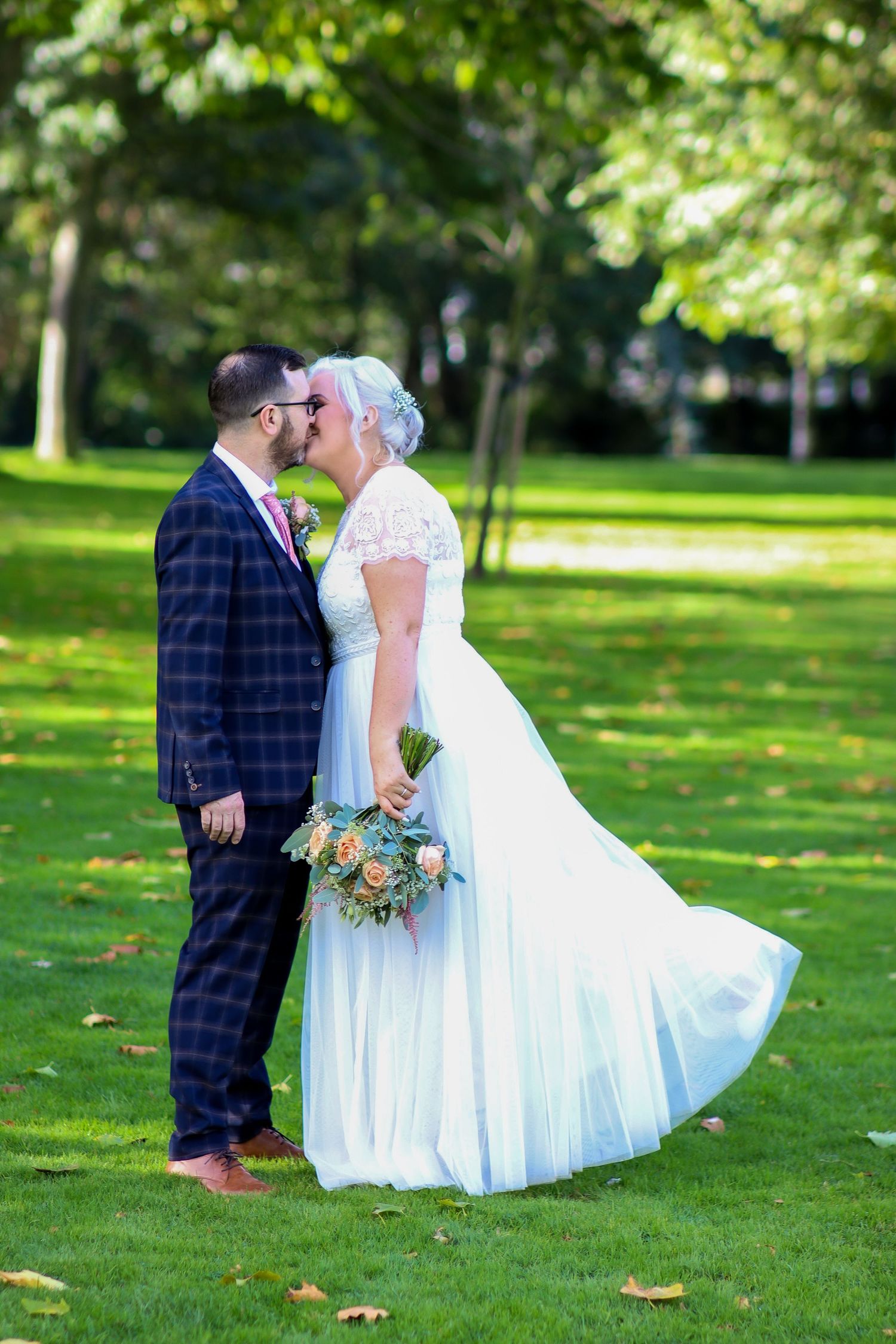 Wedding couple poses together on green lawn with autumn leaves scattered around.