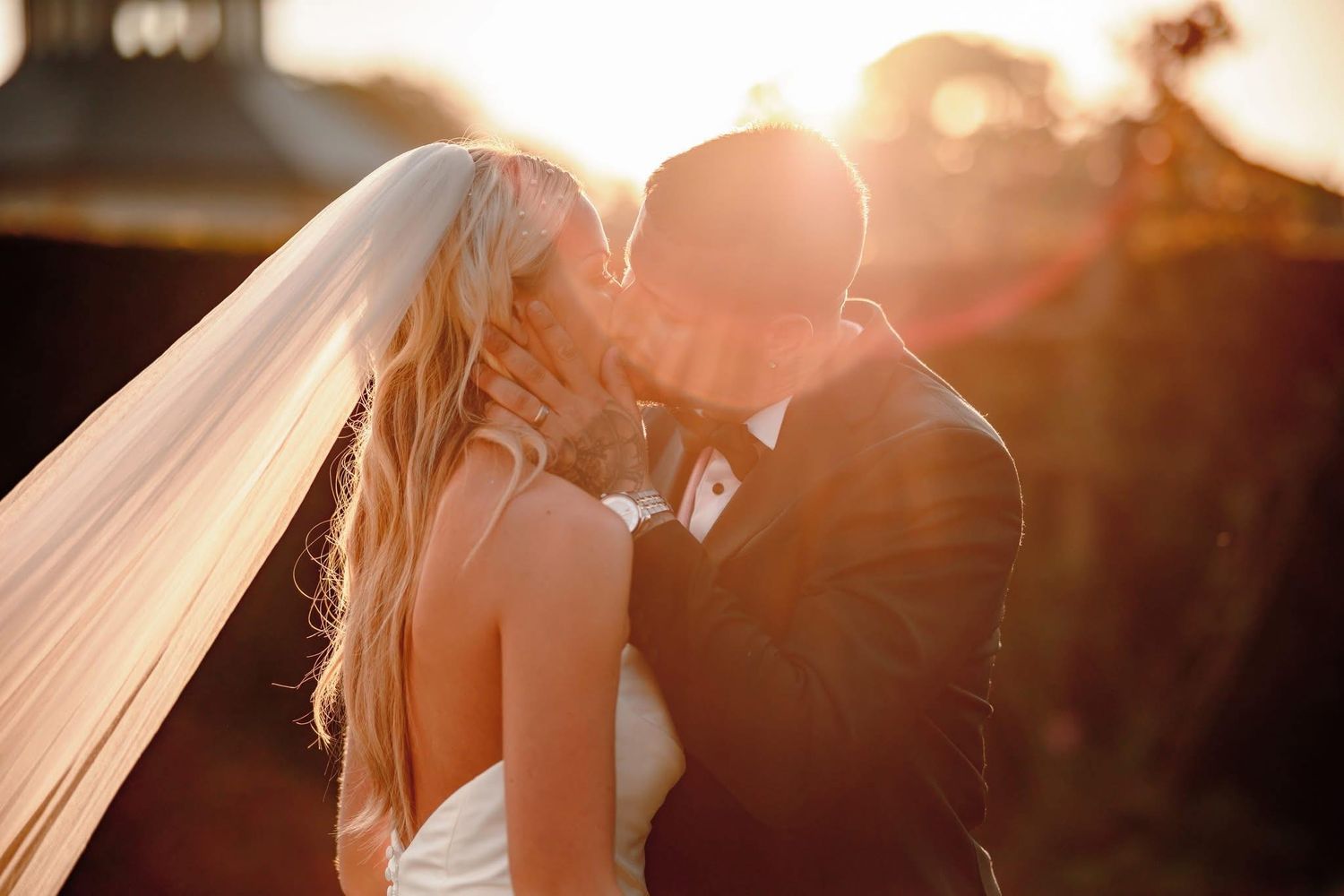Golden sunlight illuminates a romantic wedding couple moment through a delicate veil.
