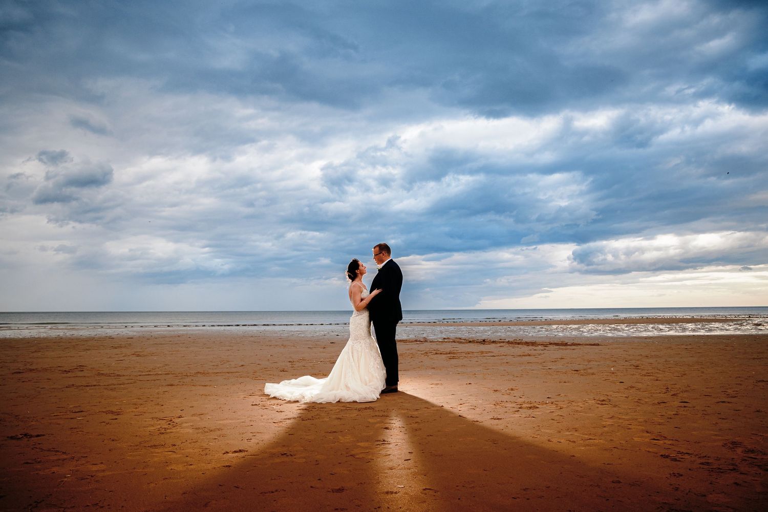 Dramatic coastal wedding photography sequence showing silhouettes against moody sky on a sandy beach at sunset.