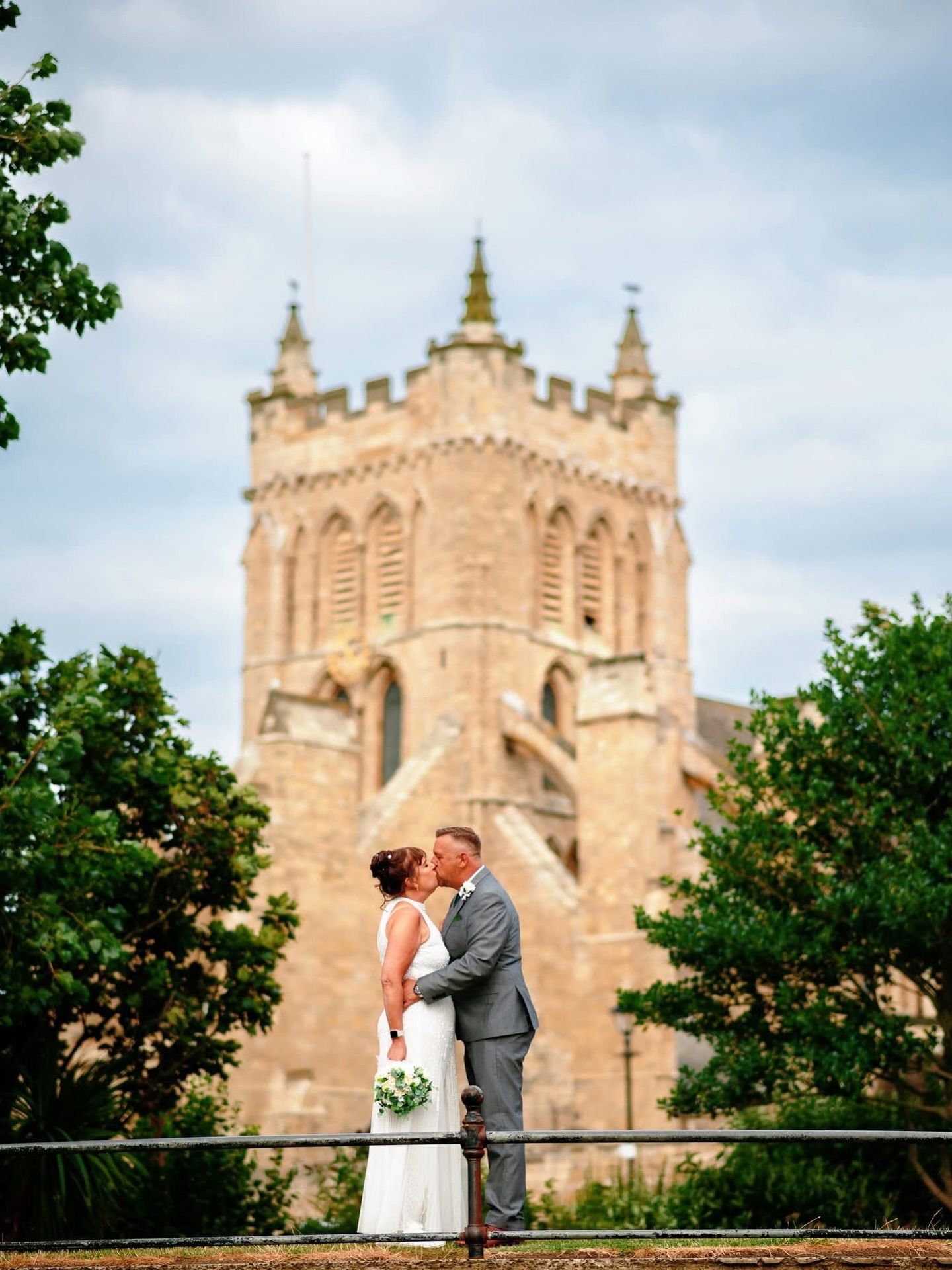 Wedding couple poses in front of historic stone church with gothic architecture.