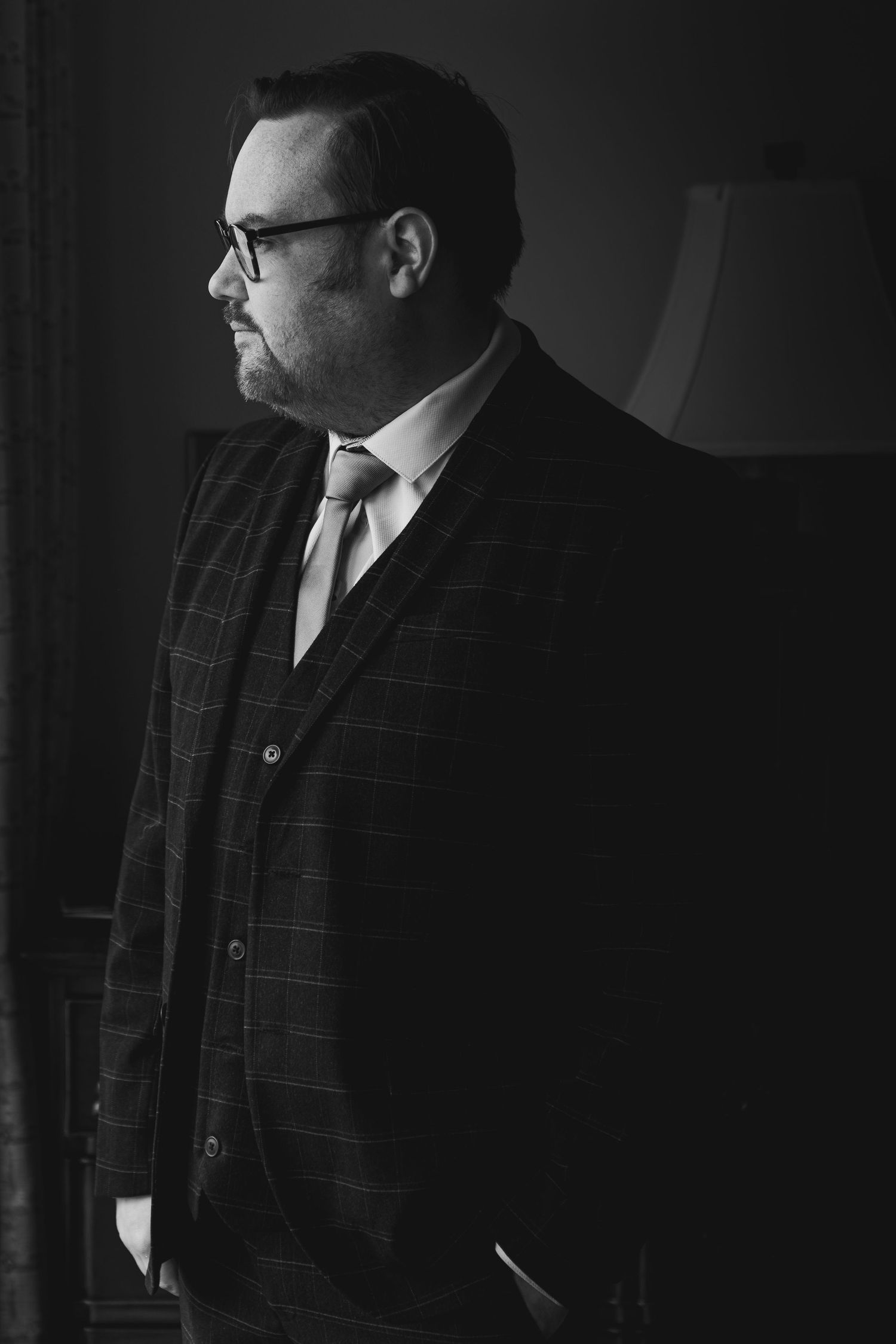 Dramatic black and white portrait series showing a person in a checkered suit and glasses against a dark background.