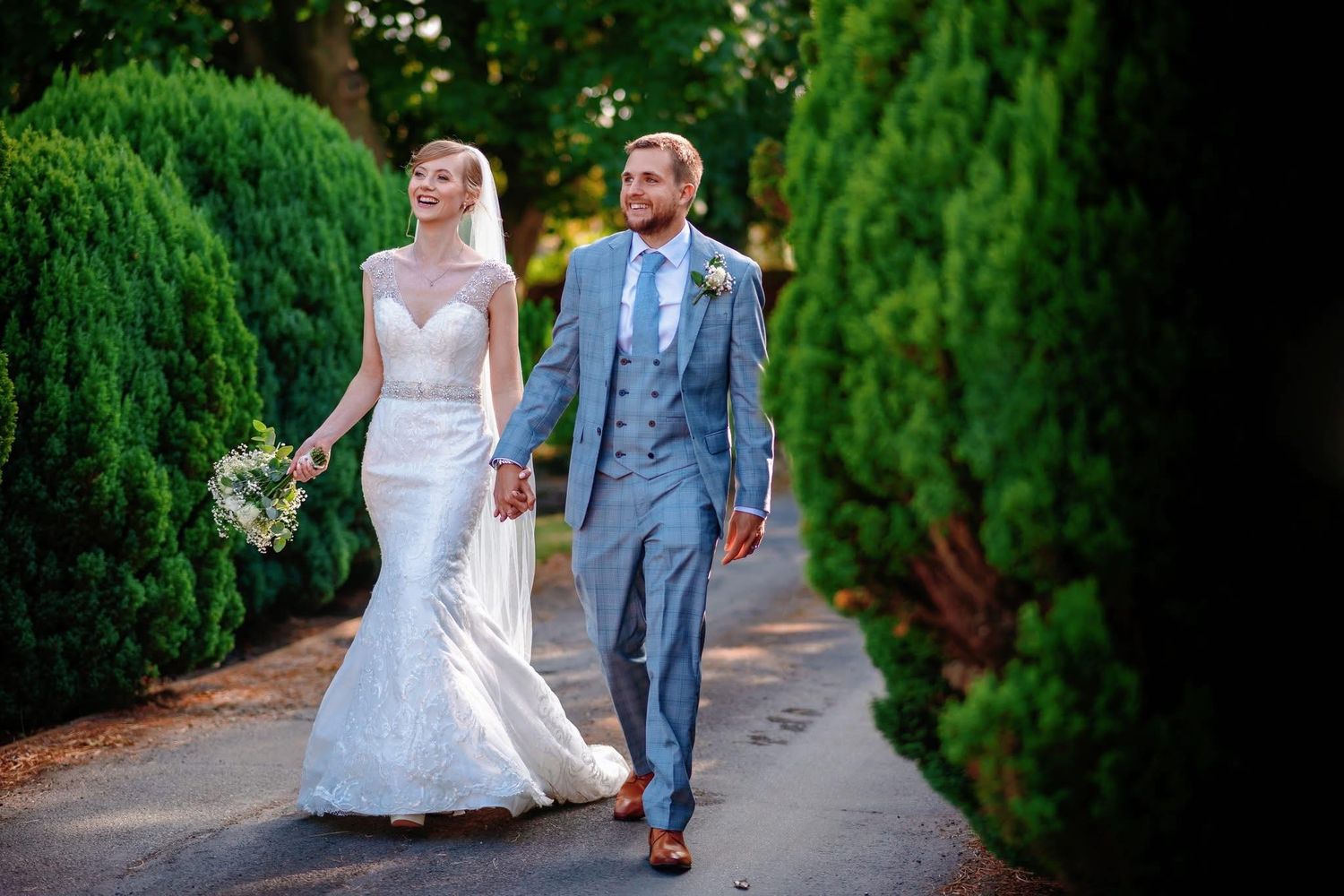 Couple walks along a garden path lined with lush green hedges.