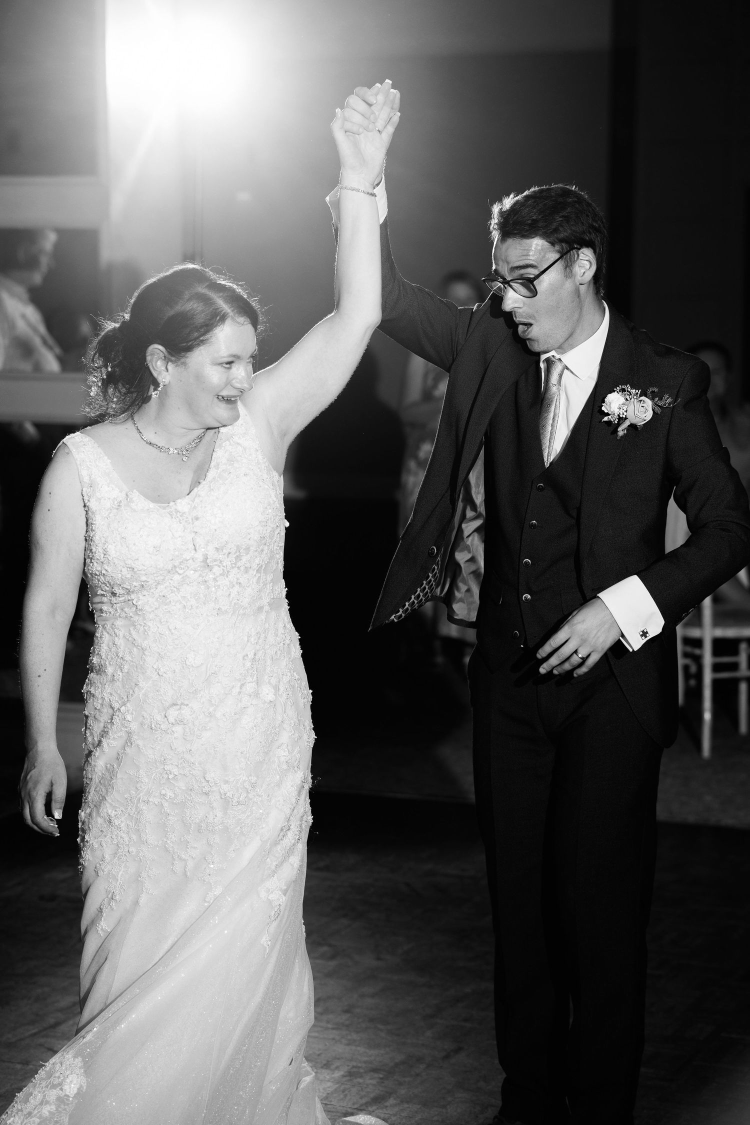 A couple dancing at their wedding reception, with the bride in a white lace dress raising her arm in celebration.