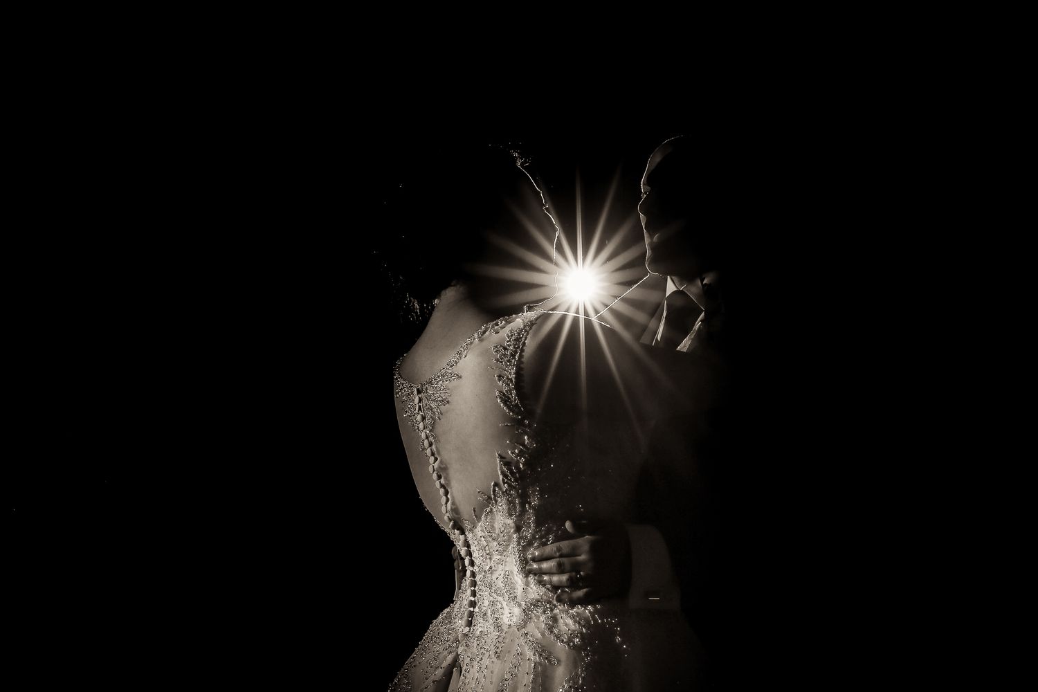 Dramatic backlit silhouette of a couple embracing during their wedding dance.