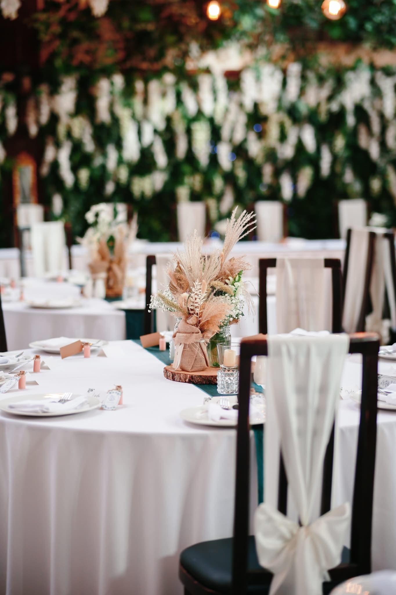 Elegant wedding reception tables set with white linens and dried floral centerpieces in a garden setting.