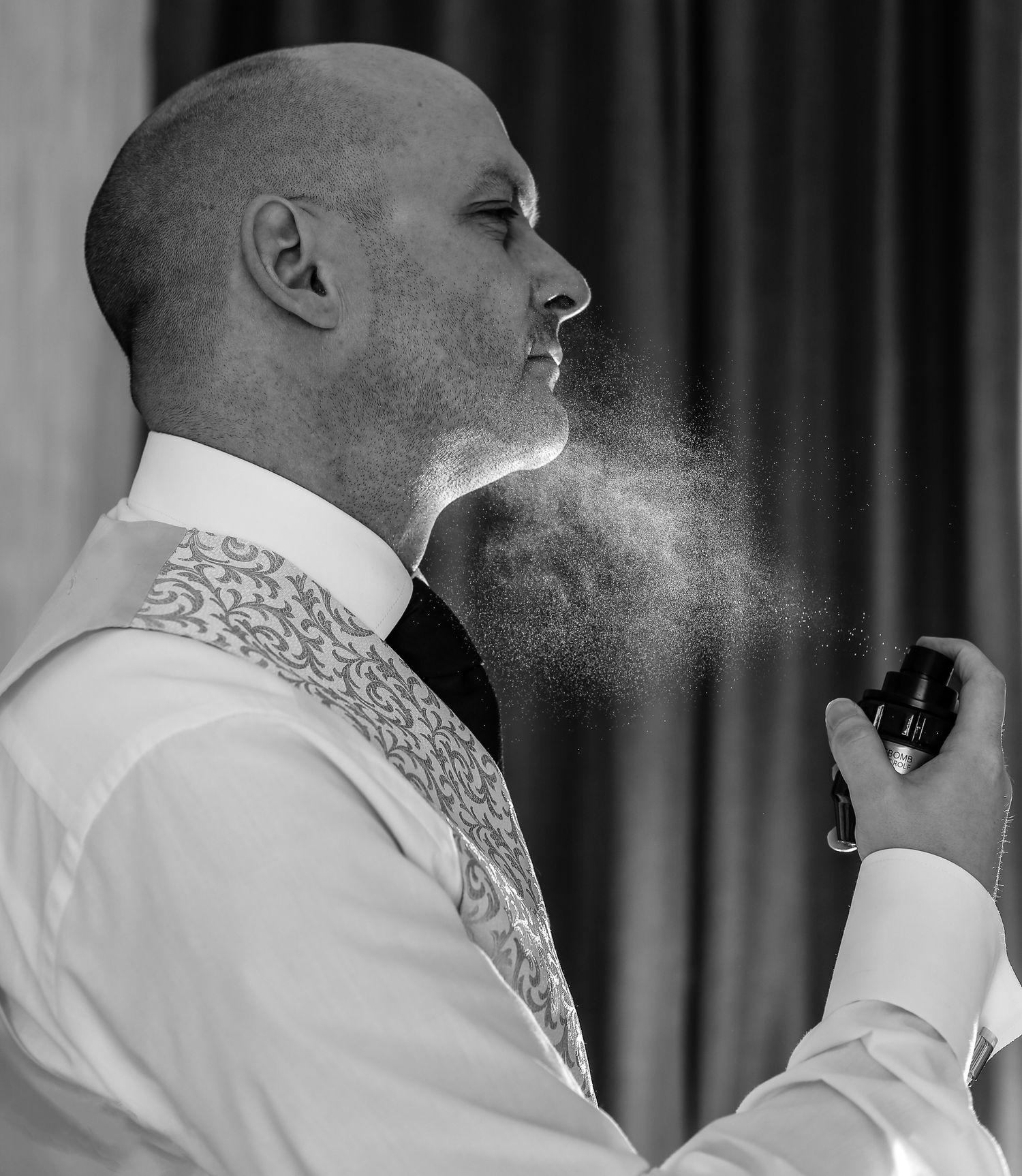 Black and white photo of someone in formal attire spraying cologne or fragrance.