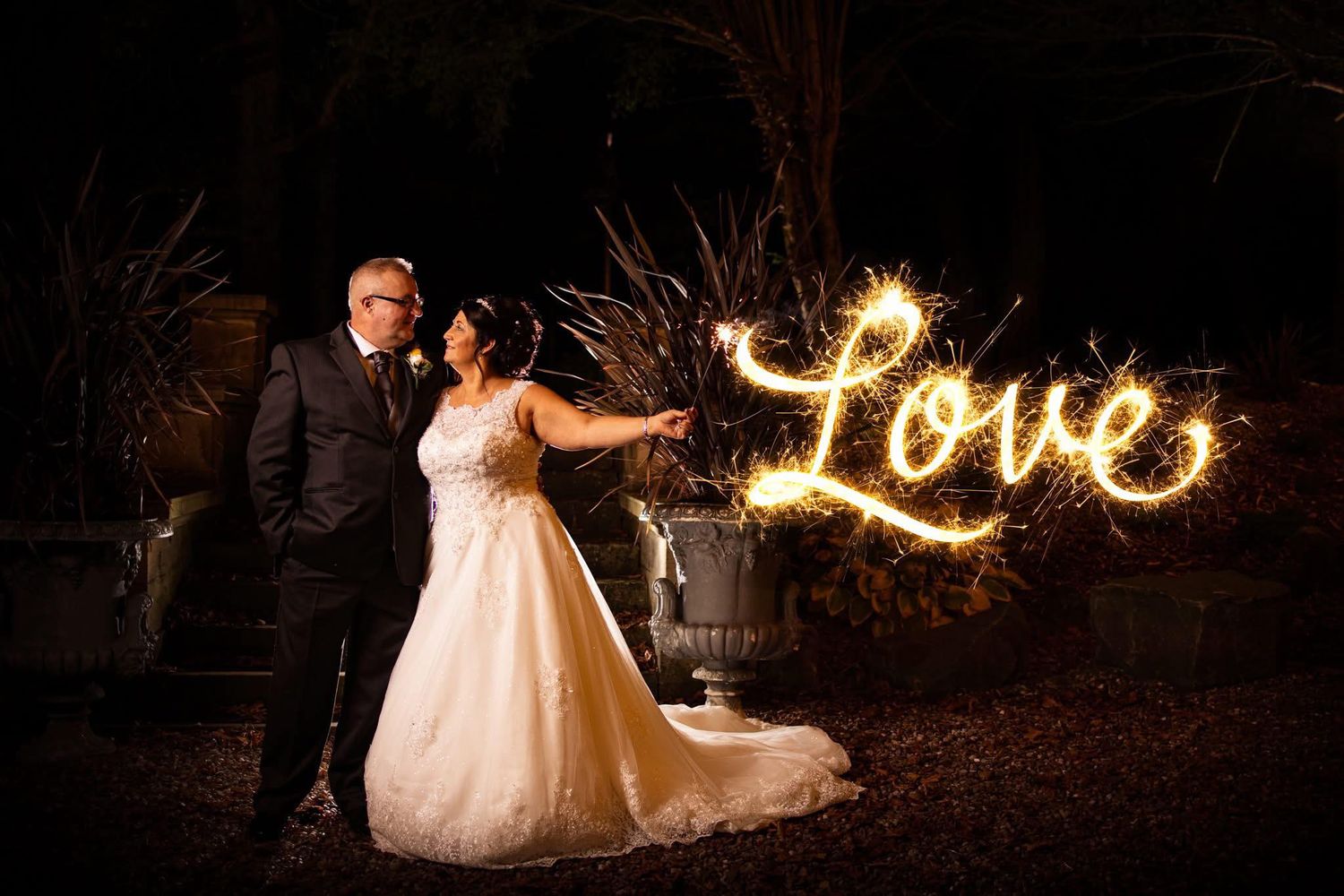 Romantic nighttime wedding photos with sparkler writing spelling 'Love' in the darkness.