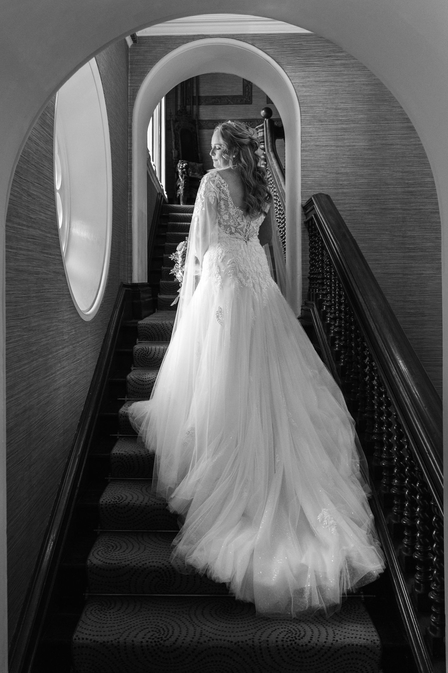A sequence of black and white photos showing a bride in a flowing white wedding gown descending an elegant staircase.