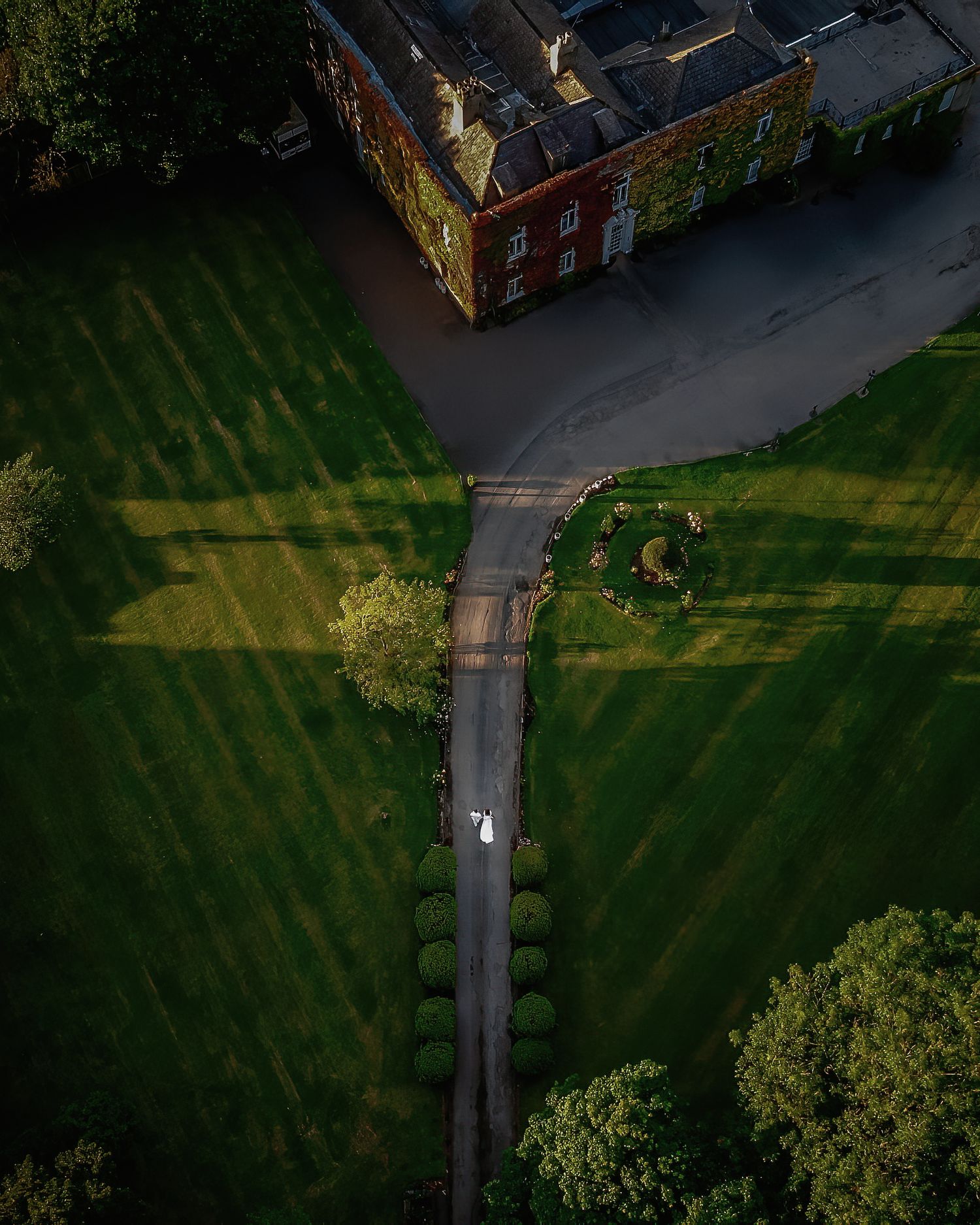 Aerial view of a winding pathway through green grass casting long diagonal shadows in evening light.