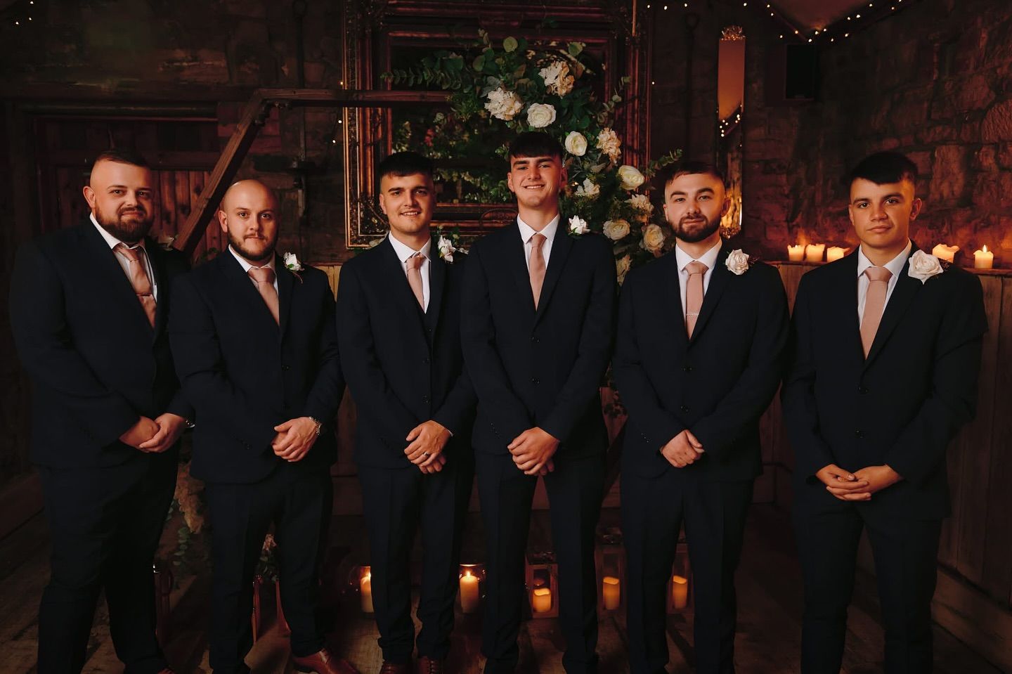 Groomsmen in dark suits line up for formal wedding party photo indoors.