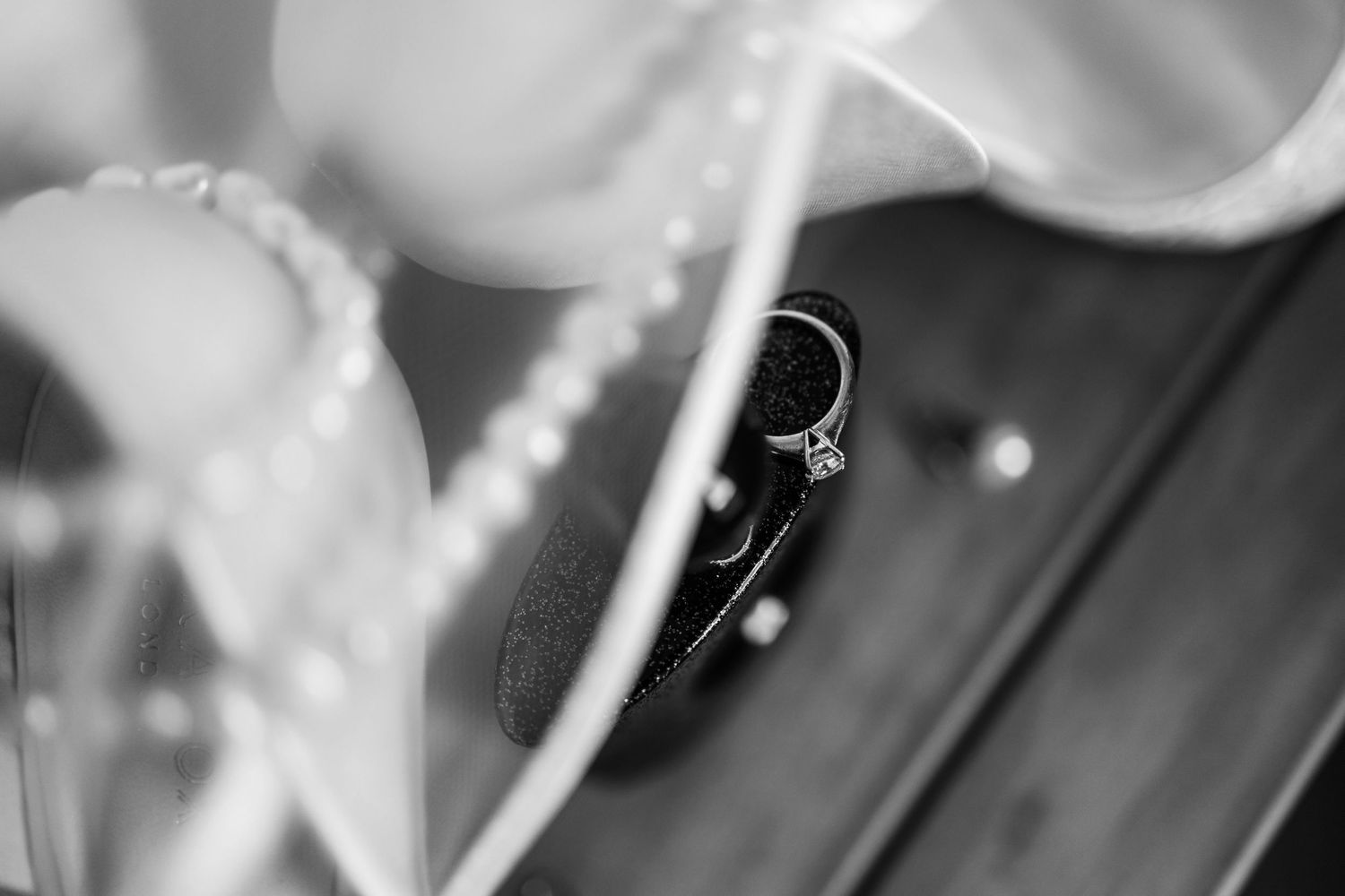 Black and white artistic macro shot of an engagement ring with soft fabric in the background.