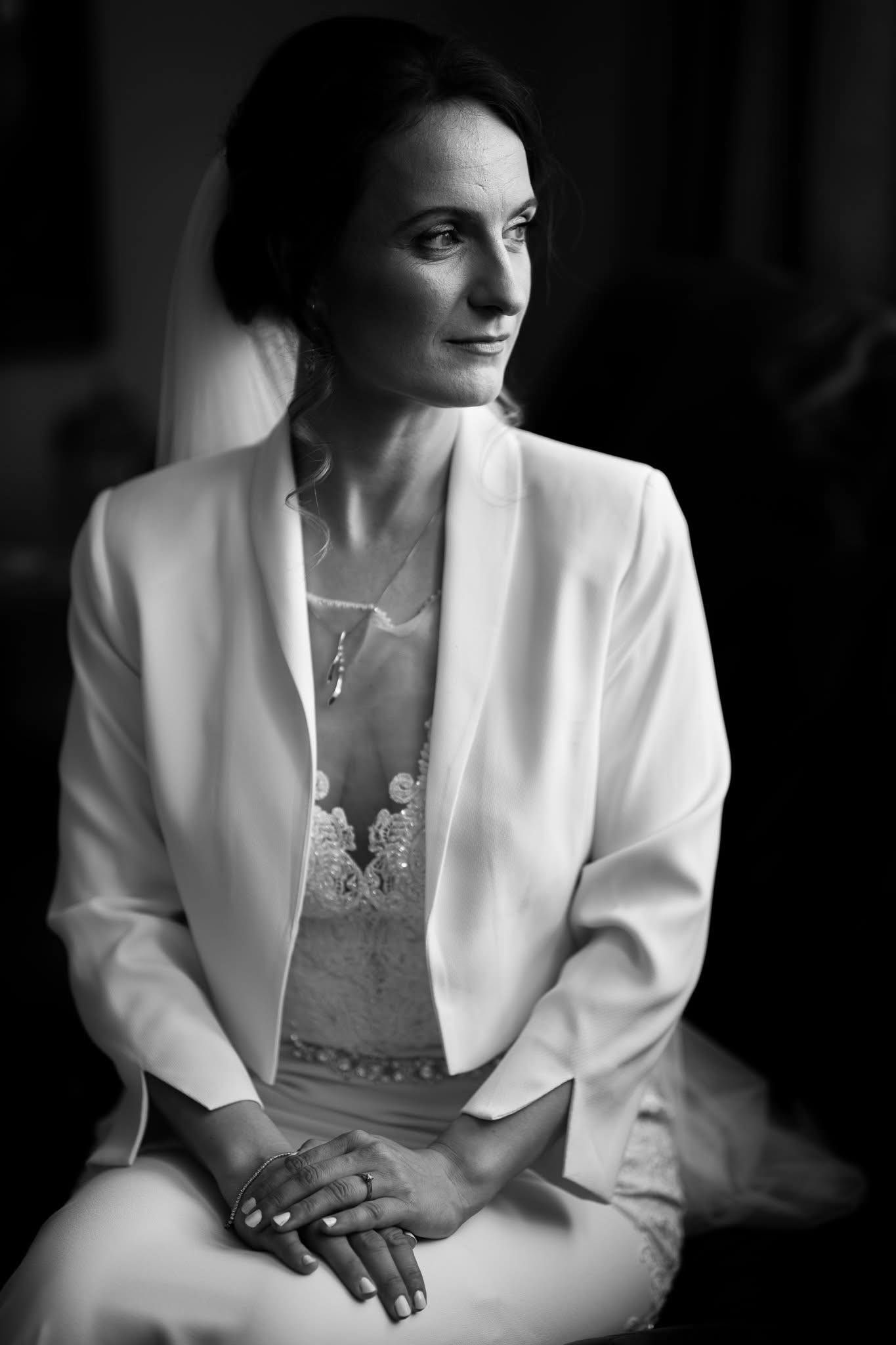 Elegant black and white portrait showing details of a white bridal blazer and lace dress.