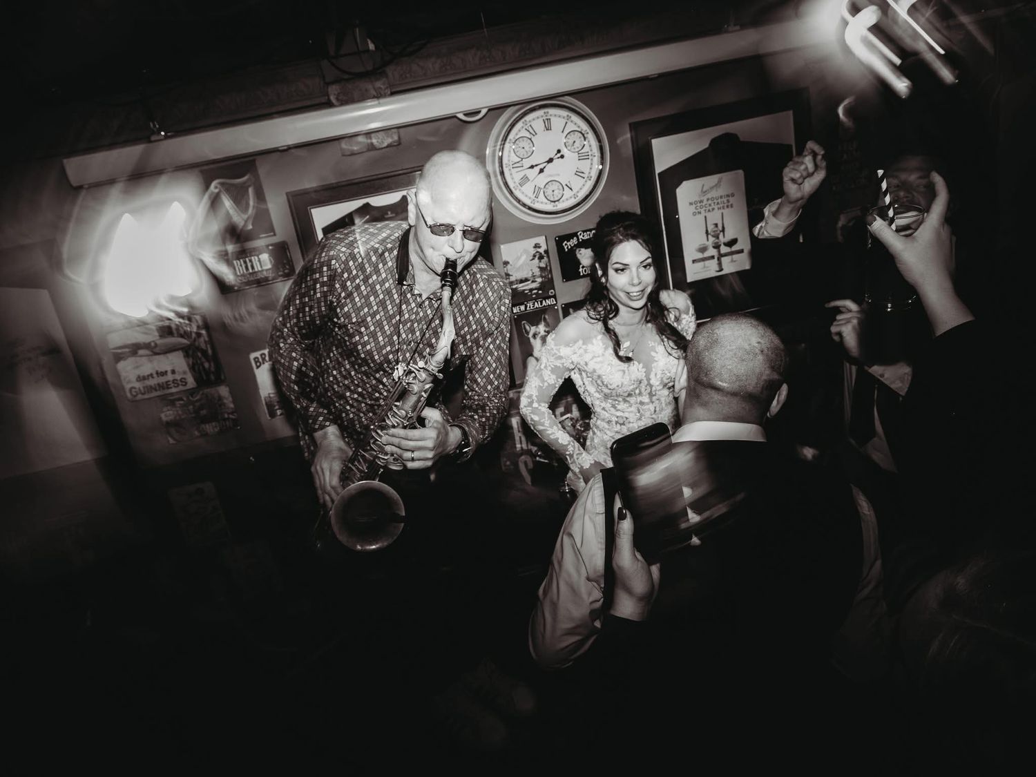 Black and white photo of guests enjoying drinks at a dimly lit wedding reception bar.