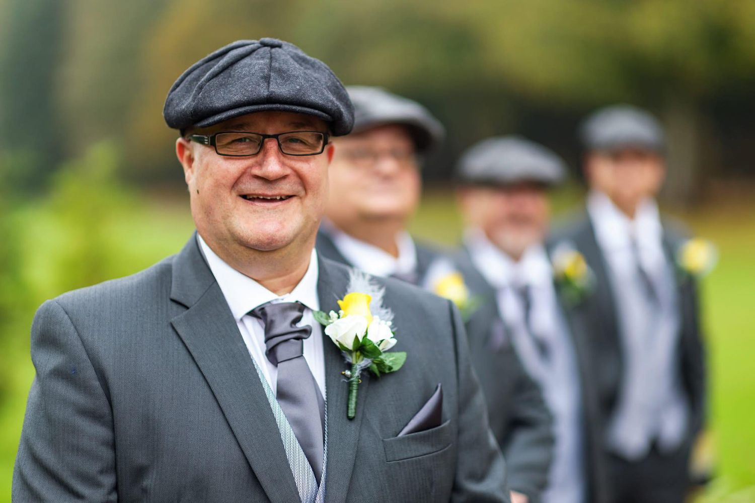Groomsmen in matching gray suits and flat caps stand together outdoors.