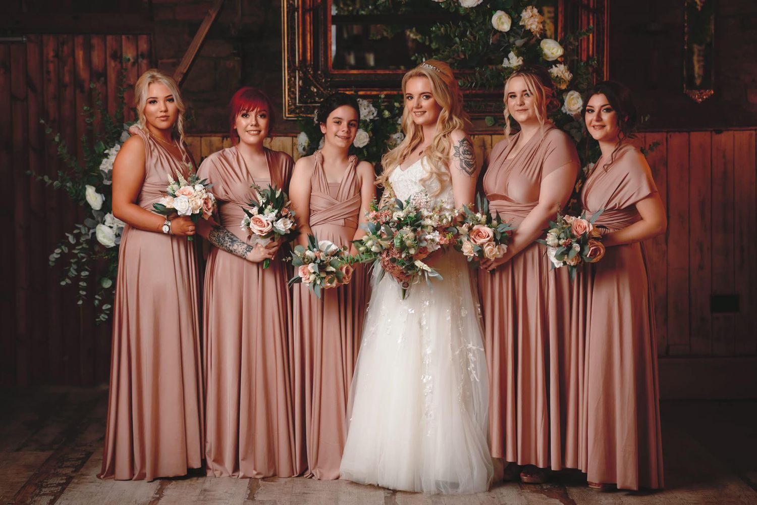 Wedding party in dusty rose bridesmaid dresses posing together with the bride in white.