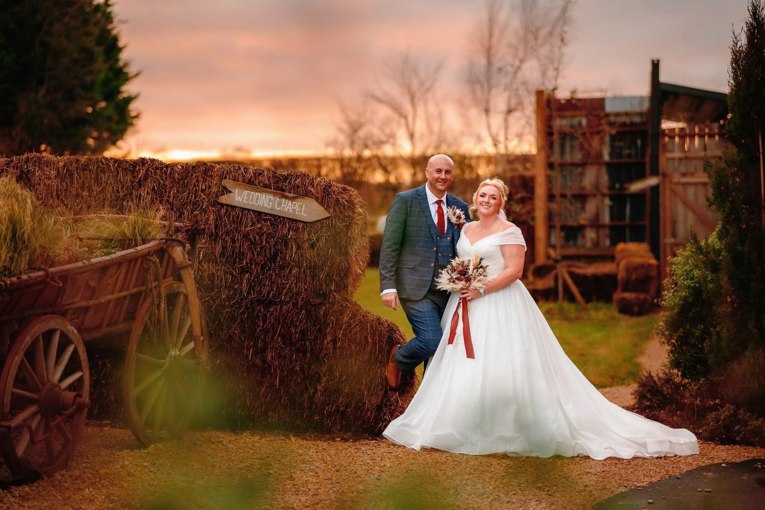 Romantic sunset wedding portrait with rustic wagon and historic building backdrop.