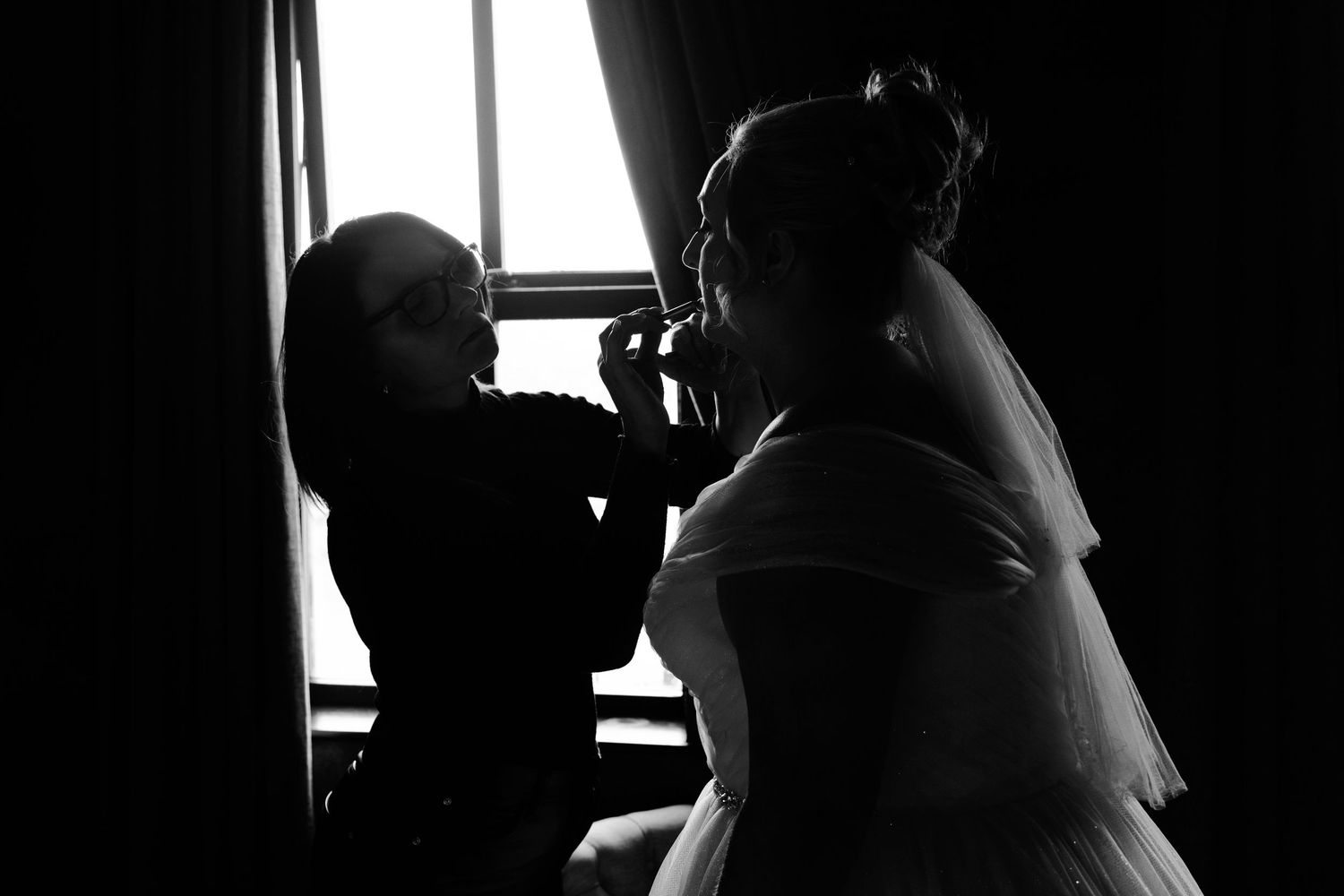 A series of silhouetted figures stand in front of windows creating a dramatic black and white composition.